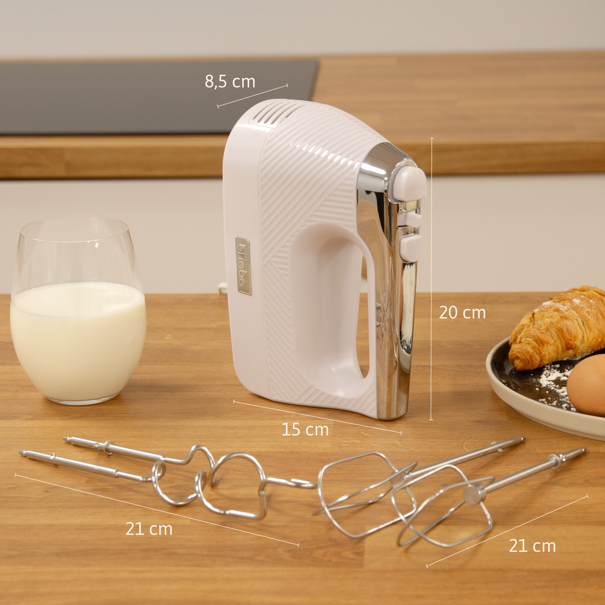 Una batidora de mano blanca con medidas. También se muestra un vaso de leche y accesorios.