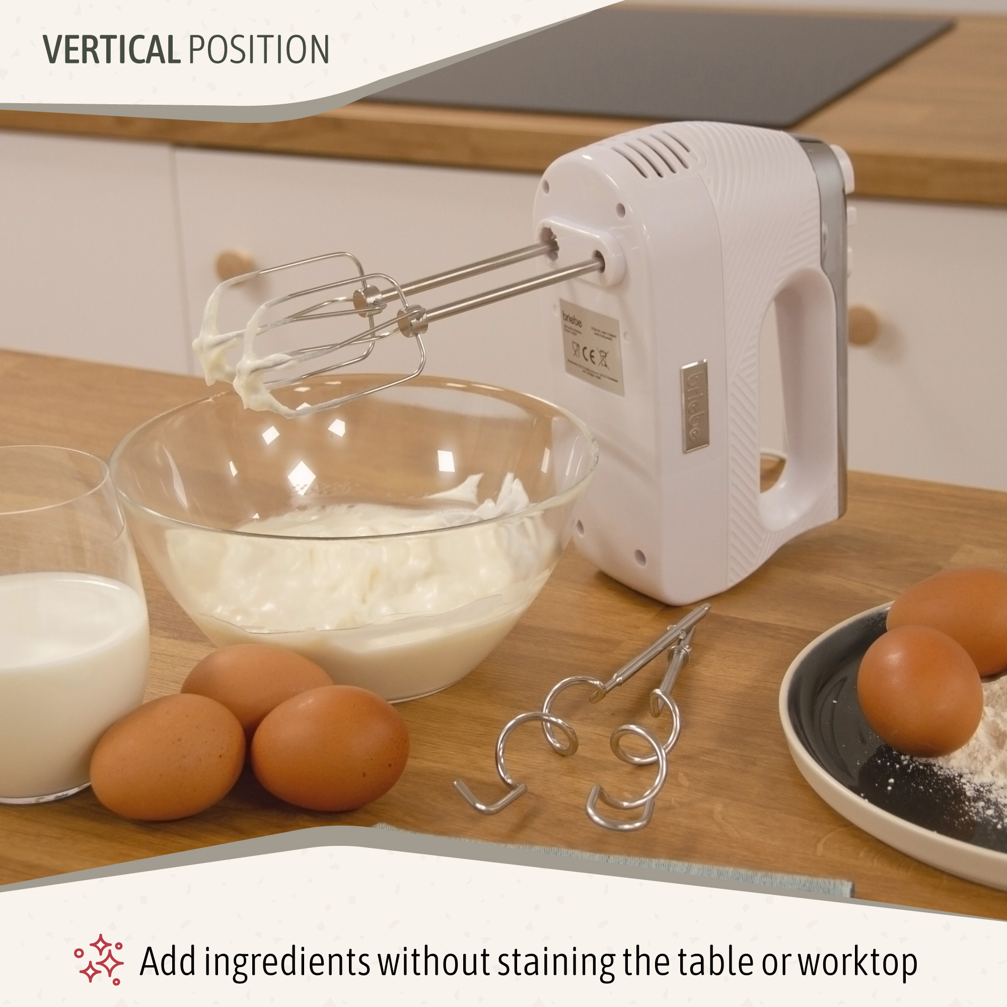 Una batidora de mano blanca está sobre un cuenco de crema. También se ven huevos, leche y harina.