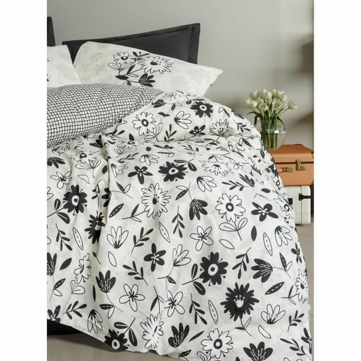 Bettwäsche-Set mit schwarz-weißen Blumenmustern. Enthält Kissen, Bettdecke und Laken, mit einem neutralen Koffer im Hintergrund.