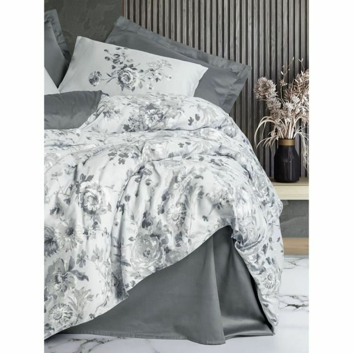 Ein Bettwäsche-Set mit grauen Blumenmustern, einschließlich Kissen, Bettdecke und Bettrock, auf grauem Hintergrund.