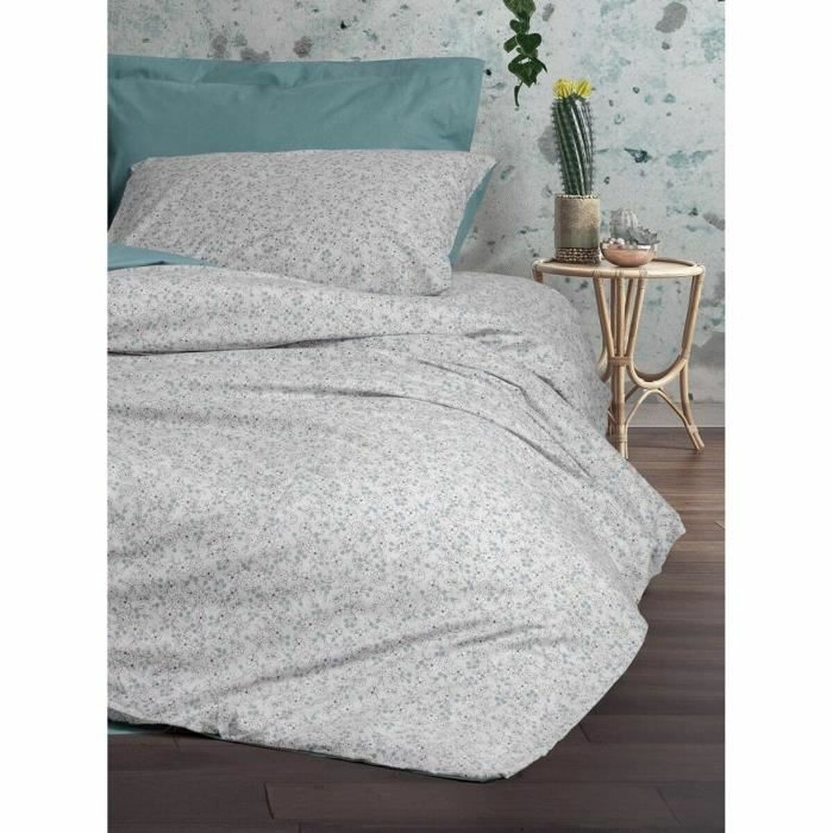 Schlafzimmer mit Bett mit floral gemusterter Bettwäsche, türkisblauem Kopfteil, kleinem Tisch und Kaktus.