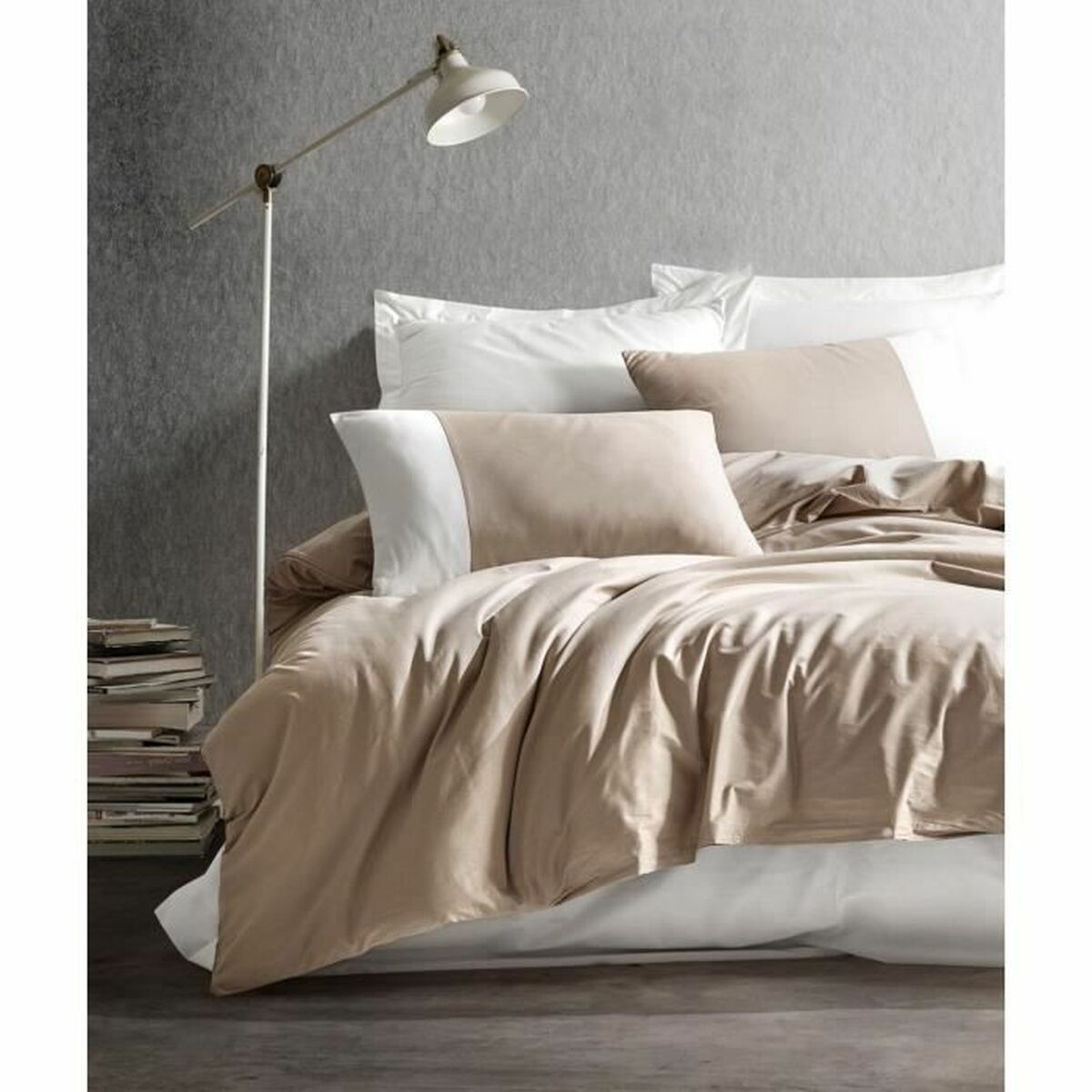 Schlafzimmer mit beiger Bettwäsche, weißen Kissen, einer Stehlampe und Büchern. Eine Pflanze im Korb.
