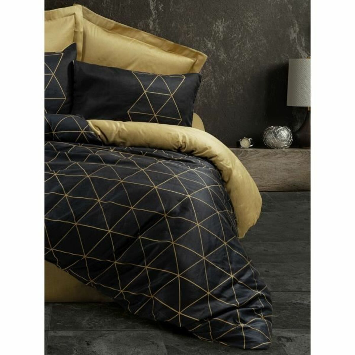 Ein Bett mit einer schwarz-goldenen, geometrisch gemusterten Bettdecke, Kissen und einem goldenen Kopfteil.