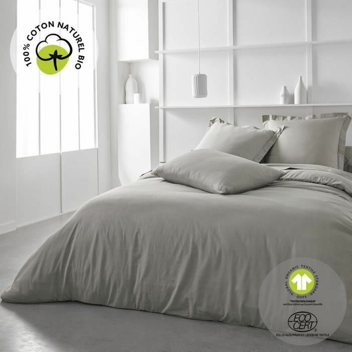 Graue Bettwäsche auf einem Bett mit Kissen und weißem Wandhintergrund, mit Öko-Zertifizierungs-Label.