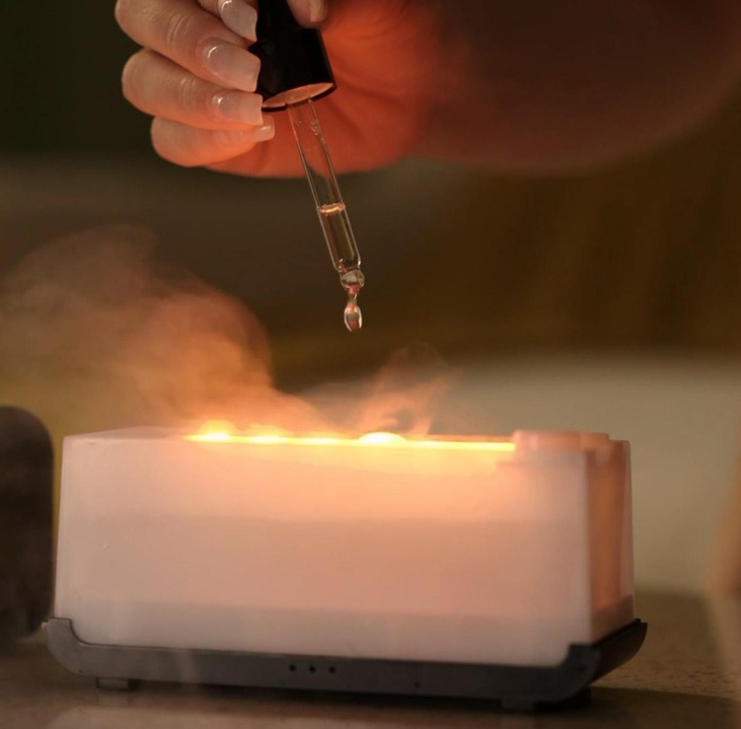 Eine Hand hält eine Pipette über einem Aromatherapie-Diffusor mit Wasser und Licht darin.
