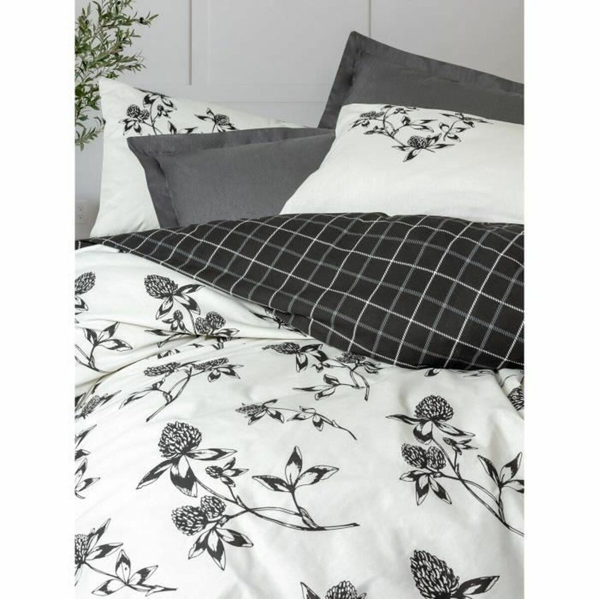Bett mit weißer Bettwäsche mit schwarzem Blumendesign und grauen Kissen.