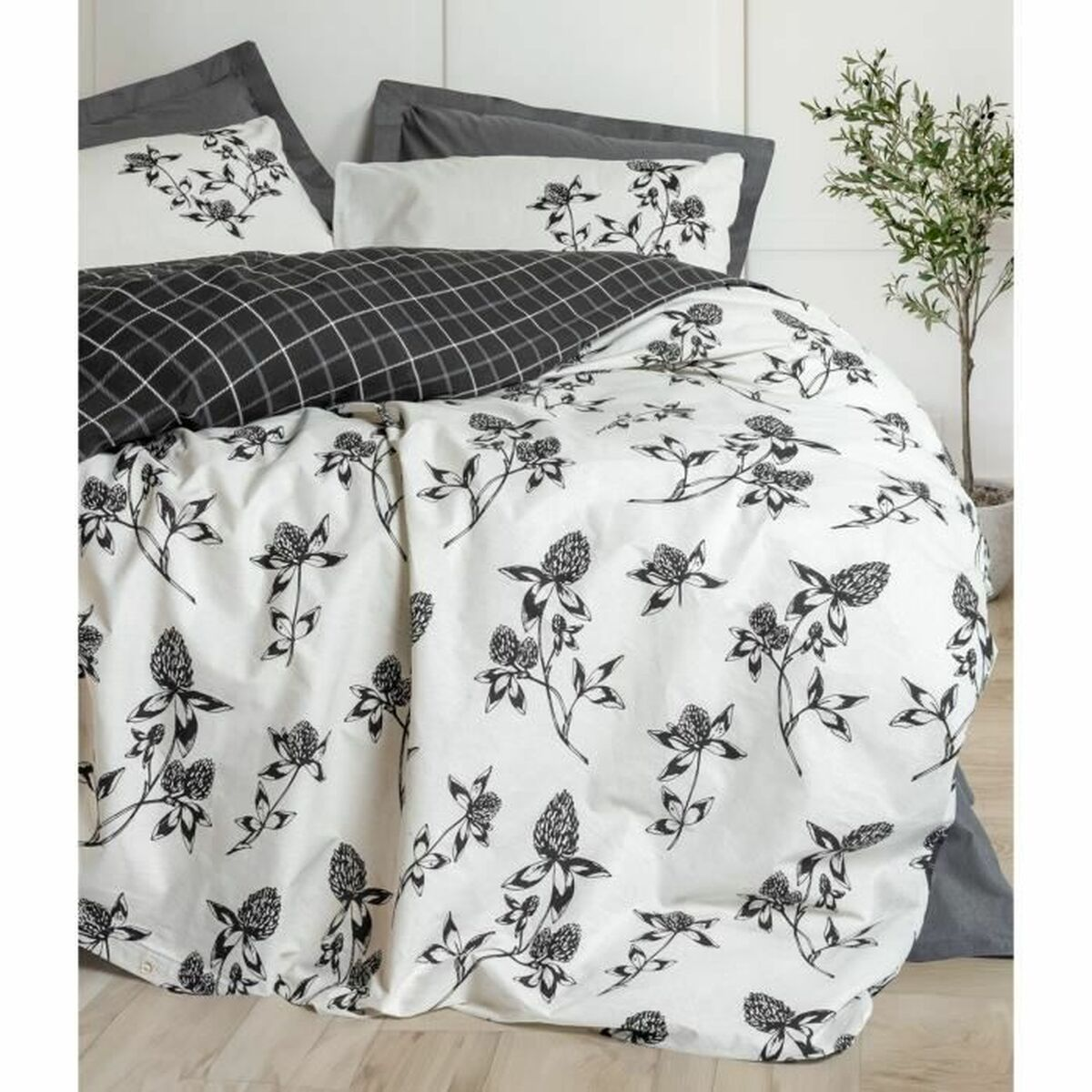 Bett mit weißer Bettwäsche, schwarzem Blumendesign, grauen Kissen und Baum im Hintergrund.