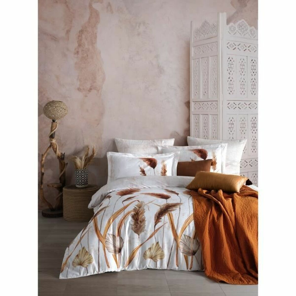 Schlafzimmer mit weißer Bettwäsche, orangefarbenem Überwurf und gemustertem Raumteiler. Erdige Töne dominieren.