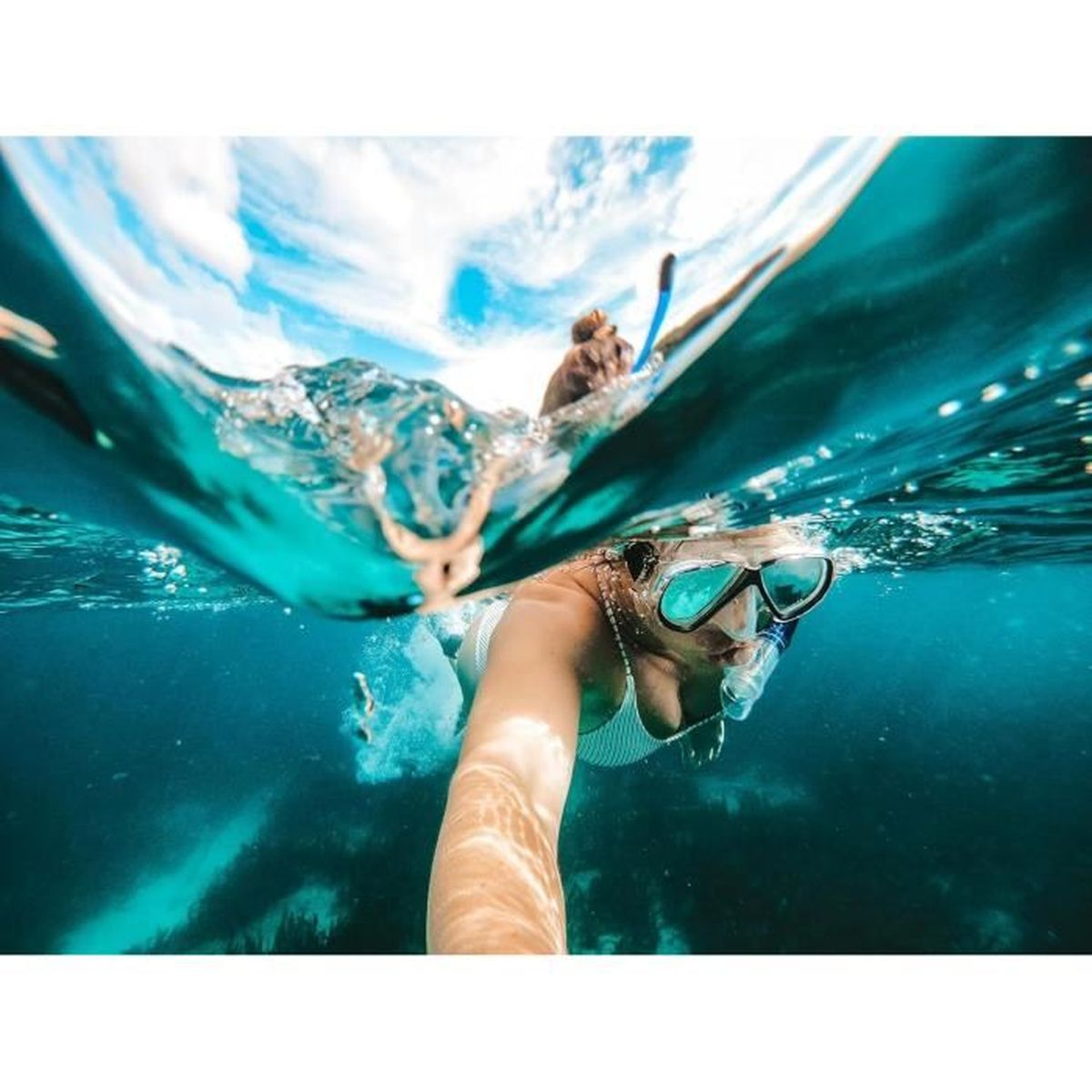 Eine Person schnorchelt unter Wasser. Eine andere Person ist in der Ferne. Das Wasser ist klar und blau.