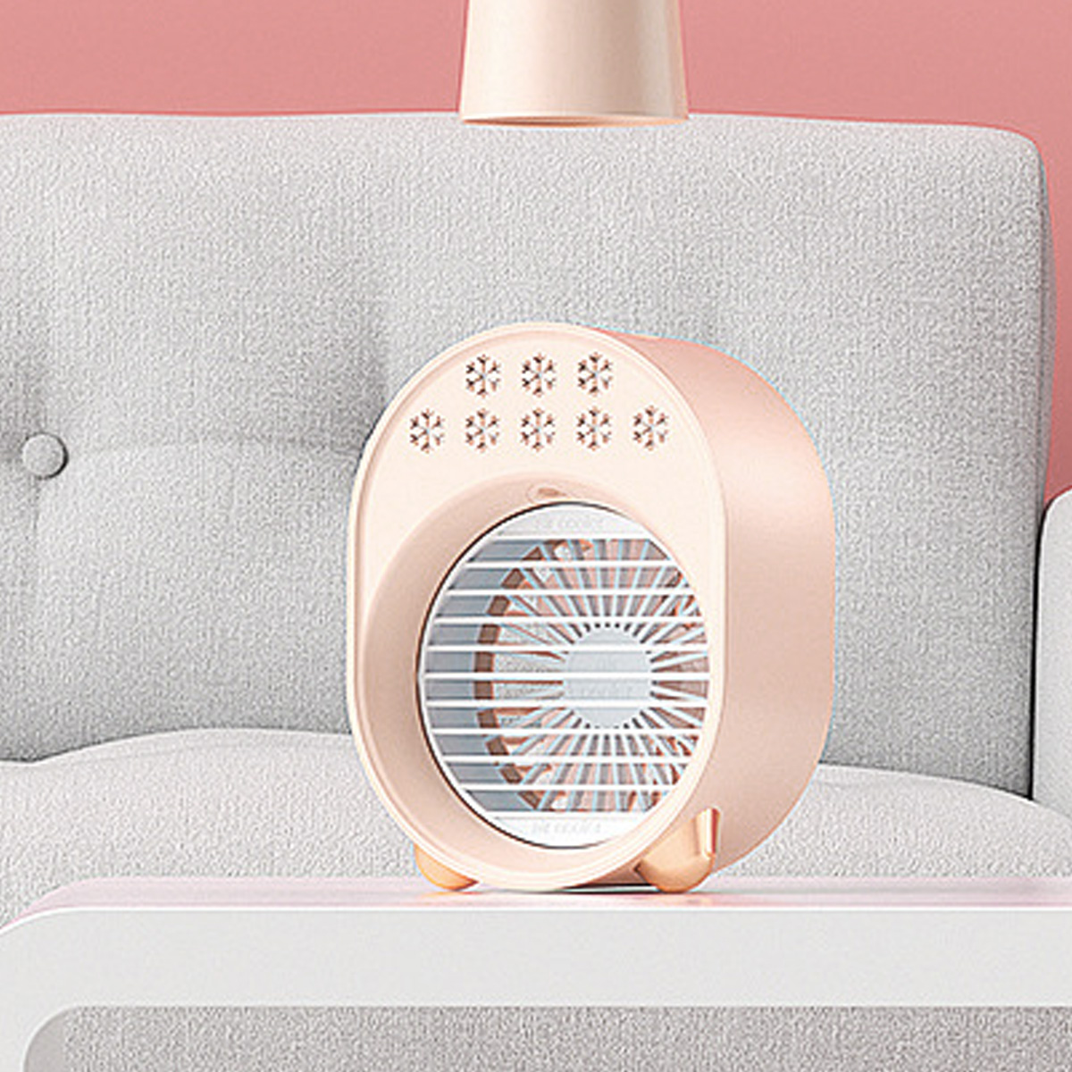 Ein rosa-weißer Luftkühler mit Ventilator, Schneeflocken-Symbolen, auf einem weißen Tisch, neben einem grauen Sofa.