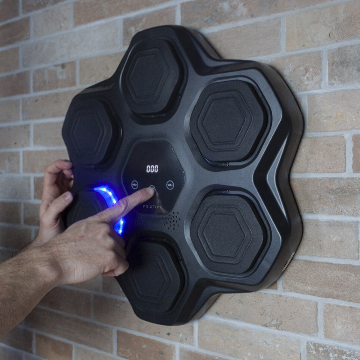 Ręka osoby naciska przycisk na czarnym elektronicznym zestawie perkusyjnym zamontowanym na ceglanej ścianie.