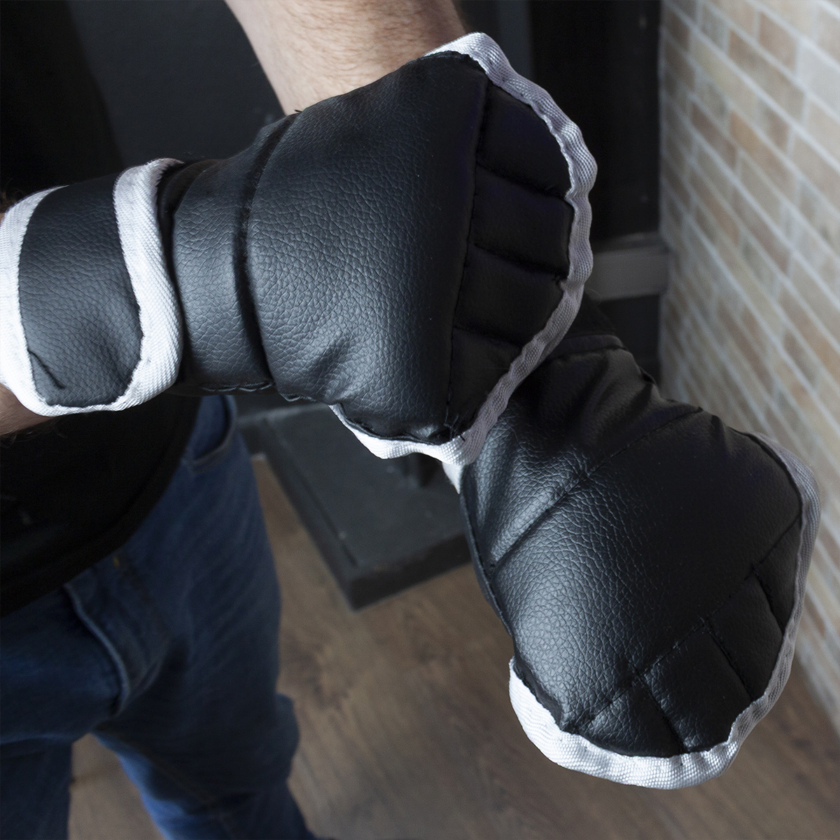 Para rękawic bokserskich w dłoniach, białe wykończenie, na tle cegieł.