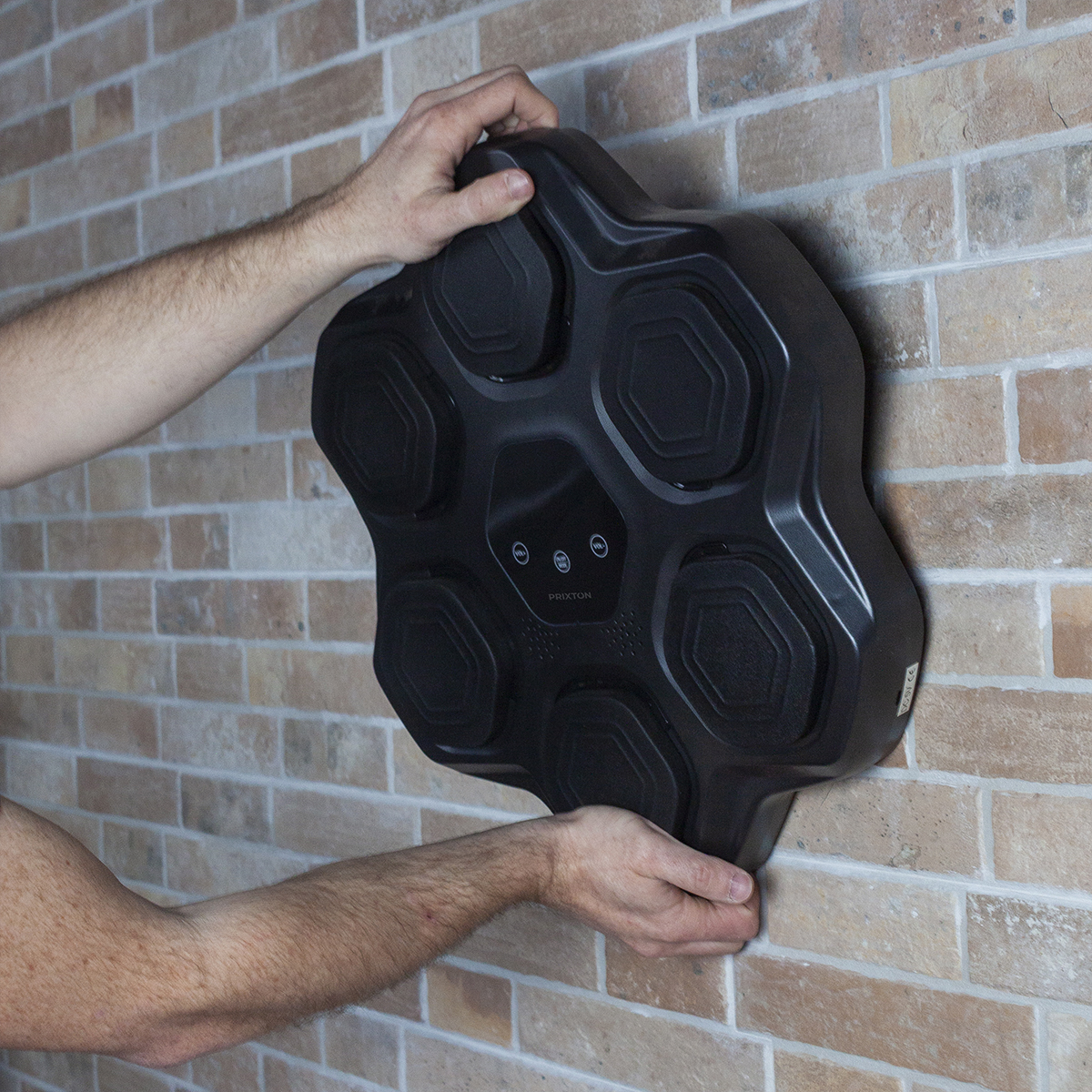 Ręce instalujące czarne urządzenie w kształcie kwiatu na ceglanej ścianie.