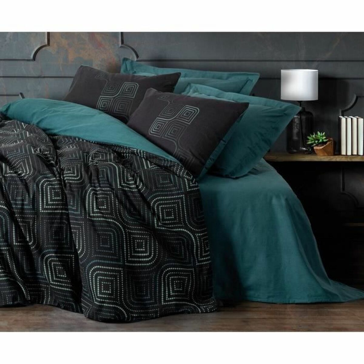 Bett mit türkisfarbenen Laken und einer schwarzen gemusterten Bettdecke und Kissen. Eine Lampe und ein Regal sind im Hintergrund.