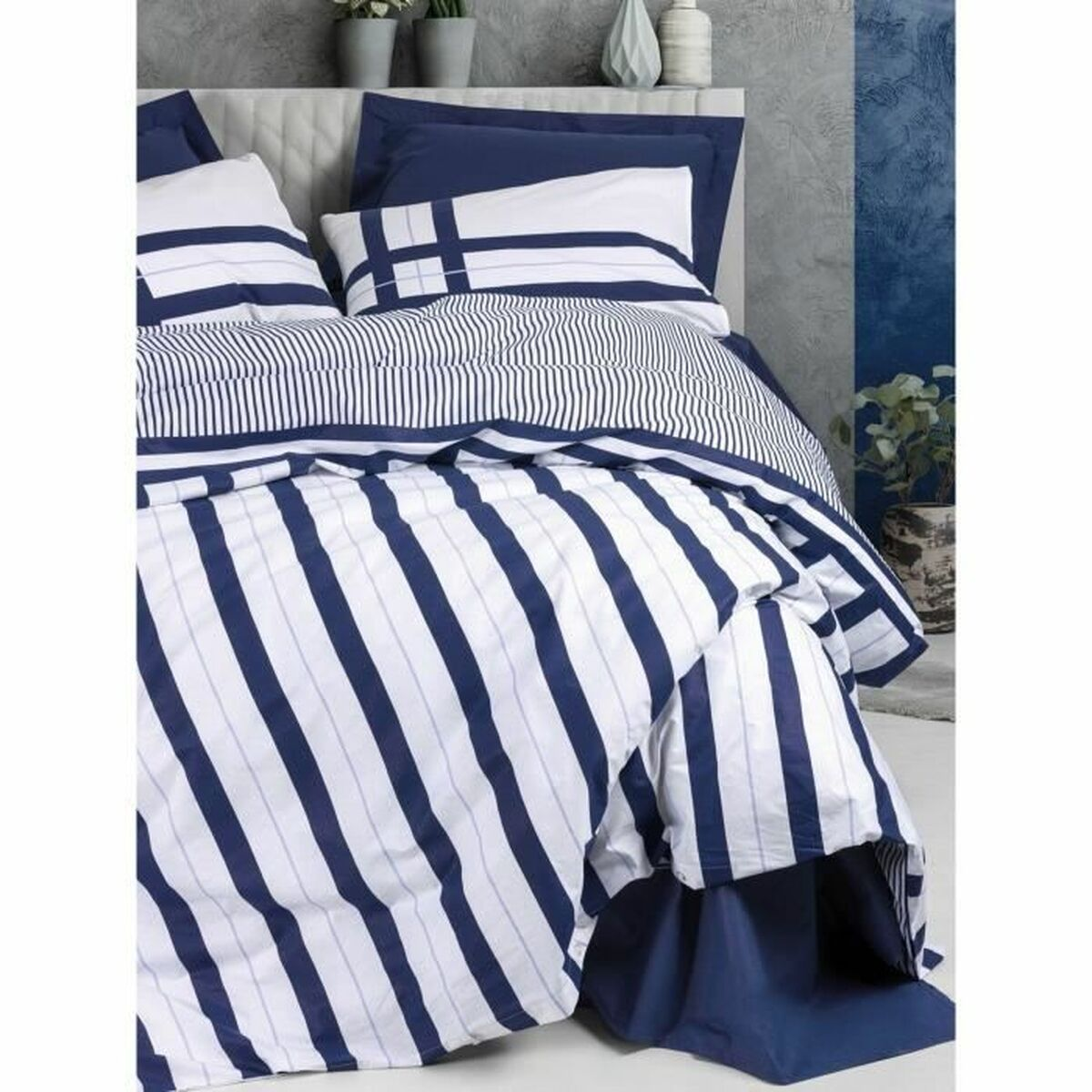 Bett mit blau-weiß gestreifter Bettwäsche, dunkelblauen Akzenten und einer Pflanze im Hintergrund.