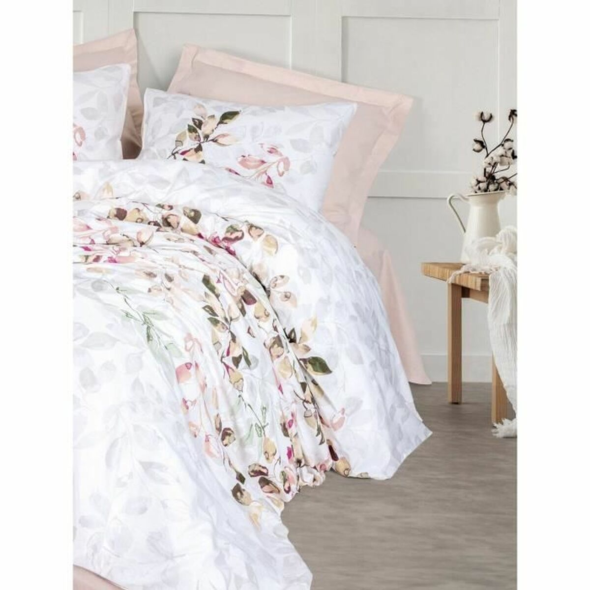 Weißes Bettwäsche-Set mit Blumenmustern. Eine weiße Kanne mit weißen Blumen und ein Holzschemel sind sichtbar.