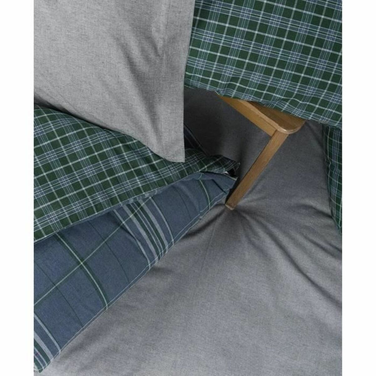 Bett mit grün karierter Bettwäsche, grauen Laken und einem Holzstuhlbein im Bild.