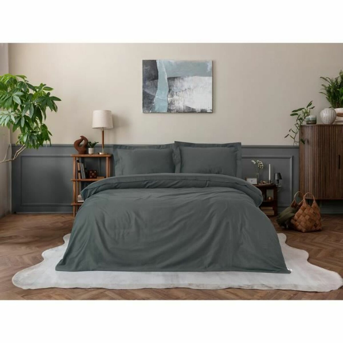 Bett mit grauer Bettwäsche, Kissen, einem Holzregal mit Büchern, einer Lampe und einer Pflanze.