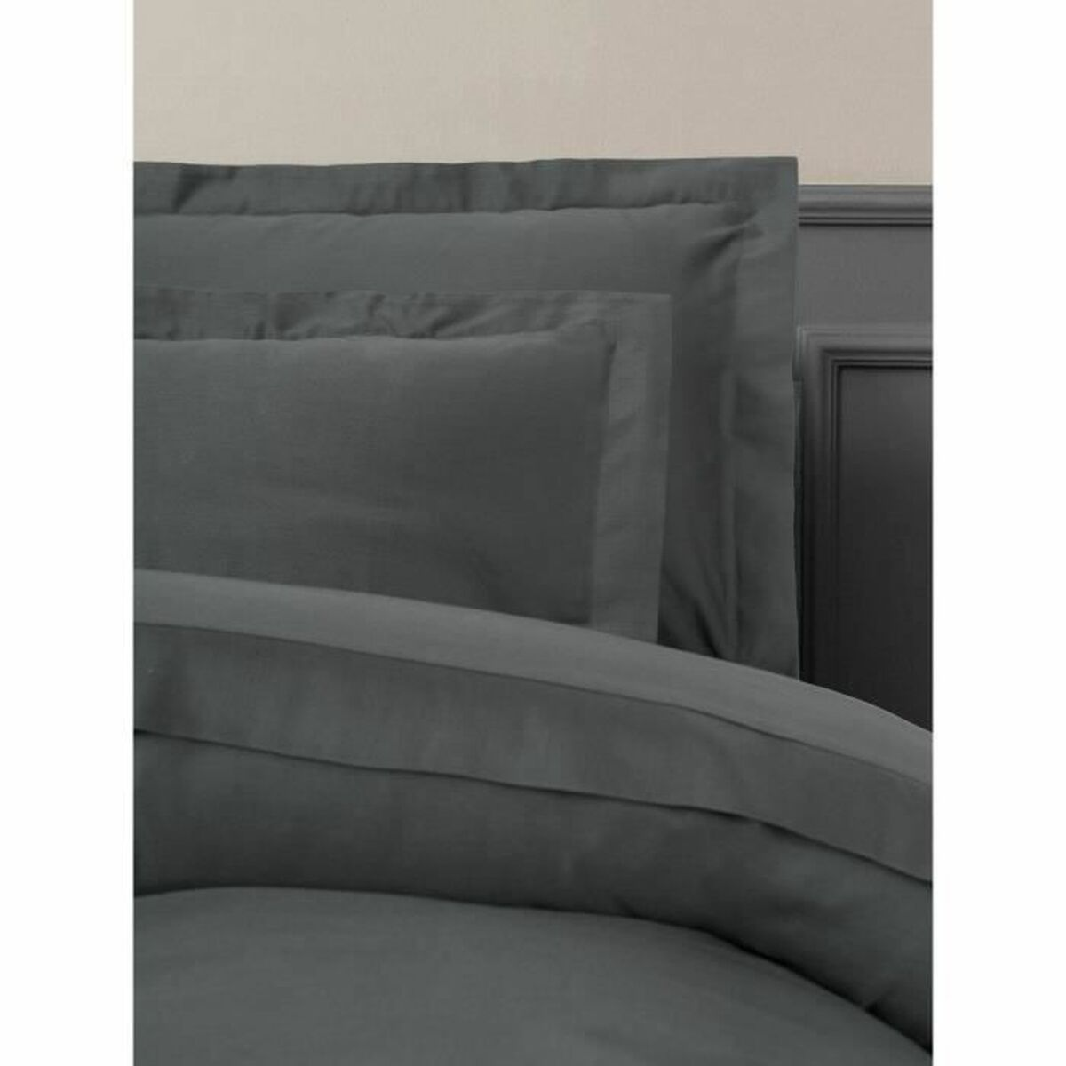 Nahaufnahme von grauen Kissen und Bettwäsche auf einem Bett, mit neutralem Hintergrund.