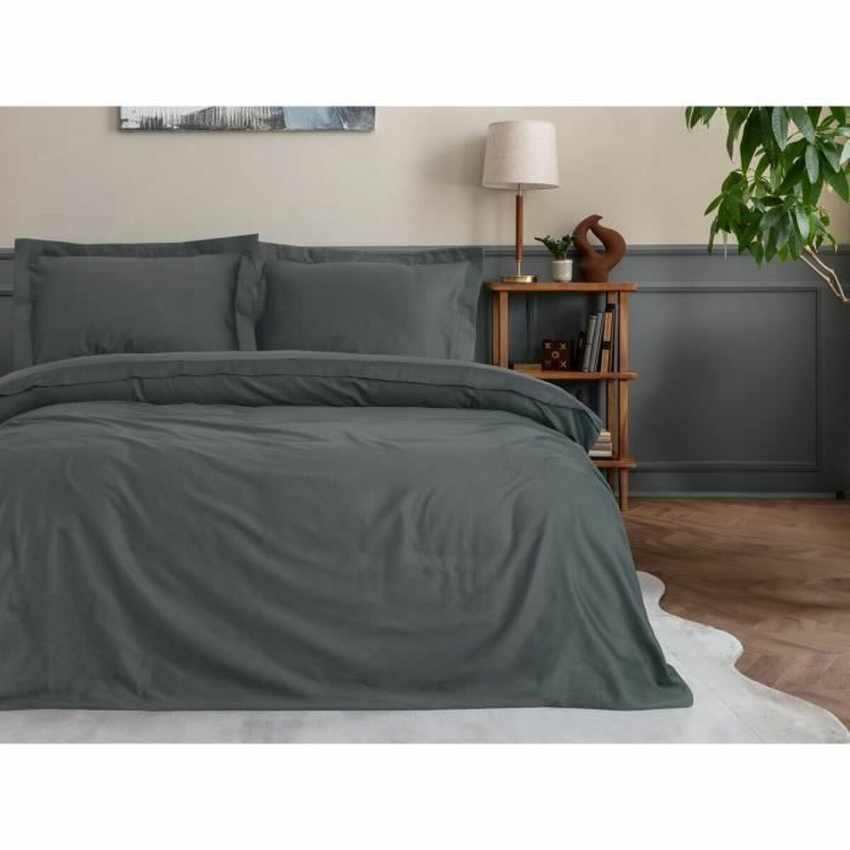 Bett mit grauer Bettwäsche, Kissen und einem Holzregal mit Büchern, einer Lampe und einer Pflanze.