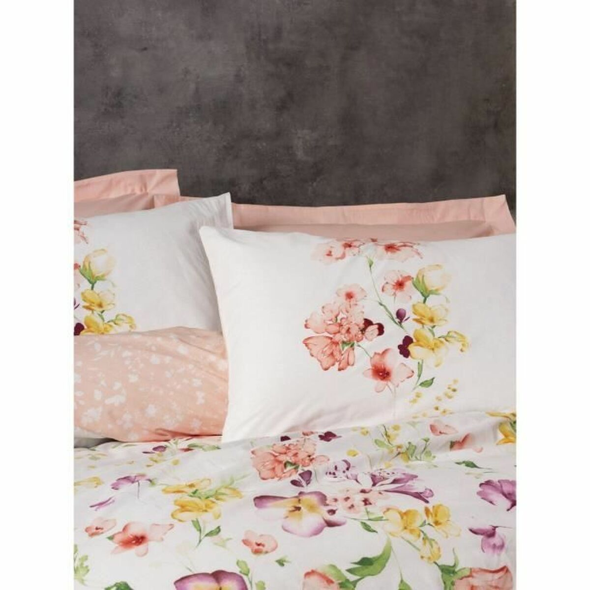 Nahaufnahme von floraler Bettwäsche auf einem Bett, mit rosa Kissenbezügen und grauem Hintergrund.