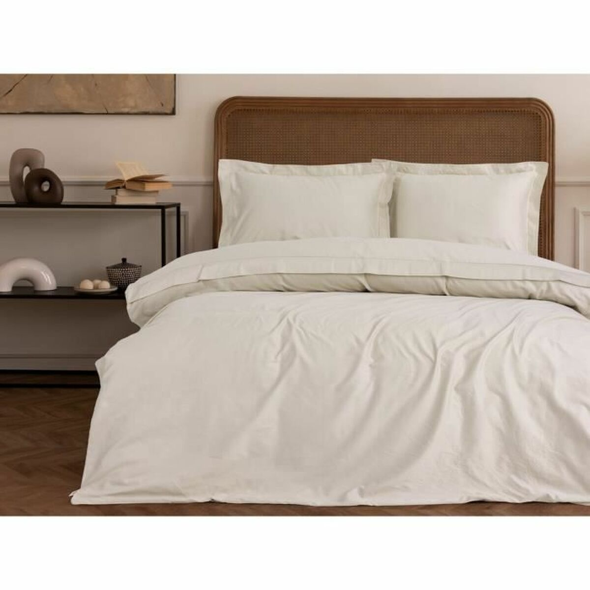 Weiße Bettwäsche auf einem Bett, mit einem Kopfende aus Korbgeflecht und einem schwarzen Tisch.