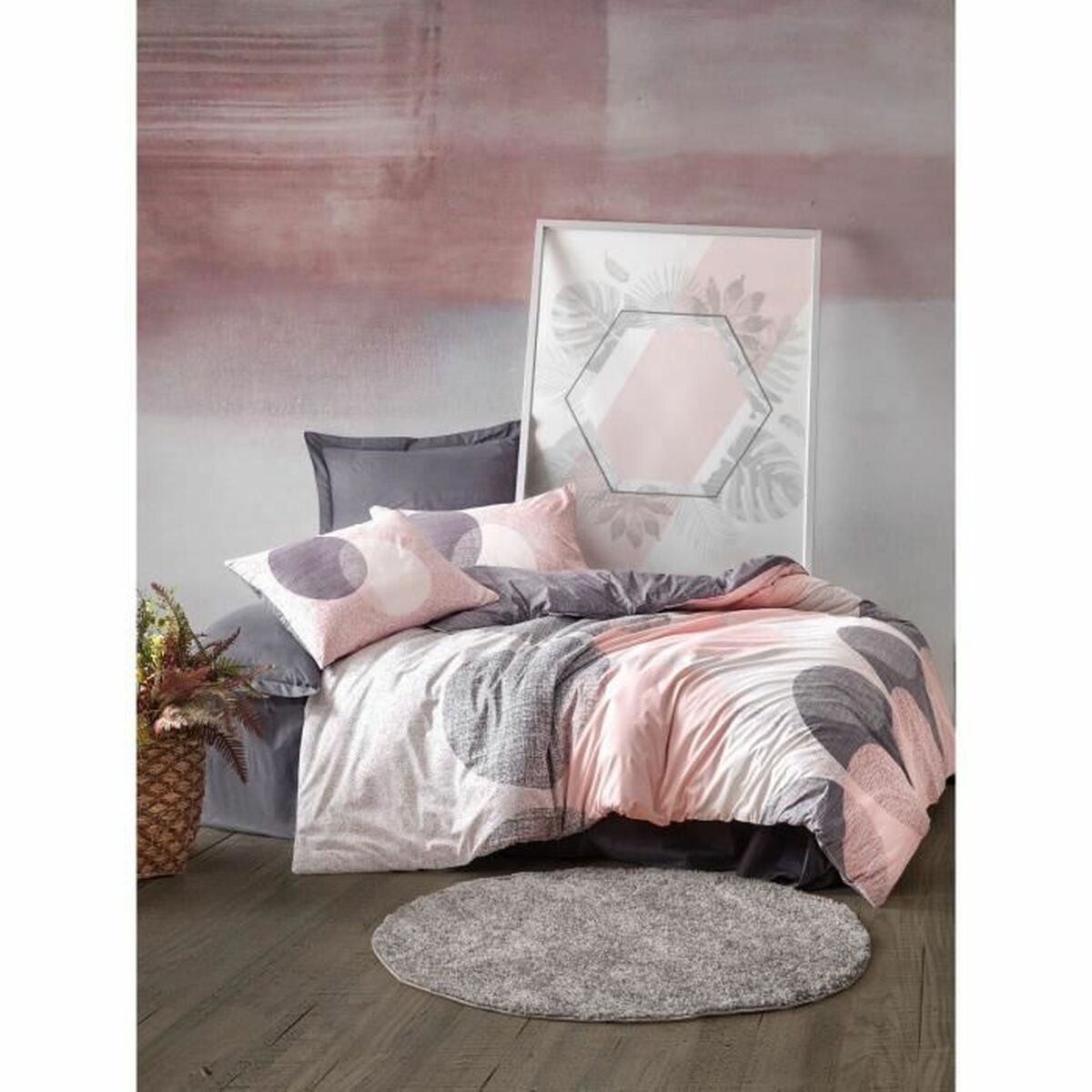Bettwäsche mit rosa und grauen Kreisen auf weißem Hintergrund, ein Bilderrahmen und ein grauer Teppich auf Holzboden.