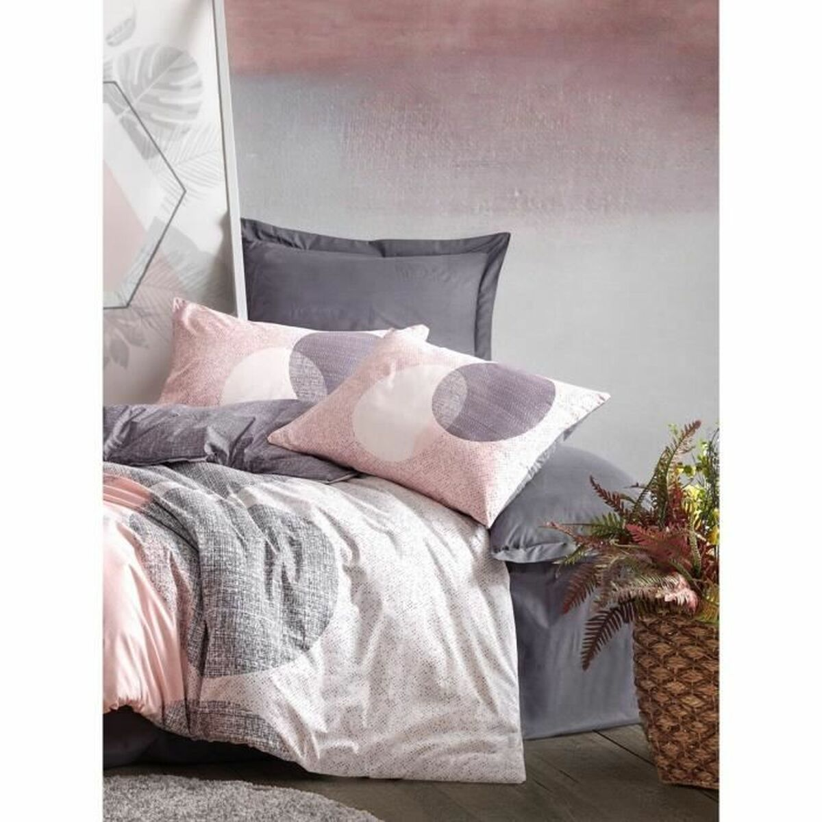 Bettwäsche-Set mit rosa und grauen Kreisen. Kissen und Bettdecke sind vorhanden. Es gibt eine Pflanze in einem Korb.
