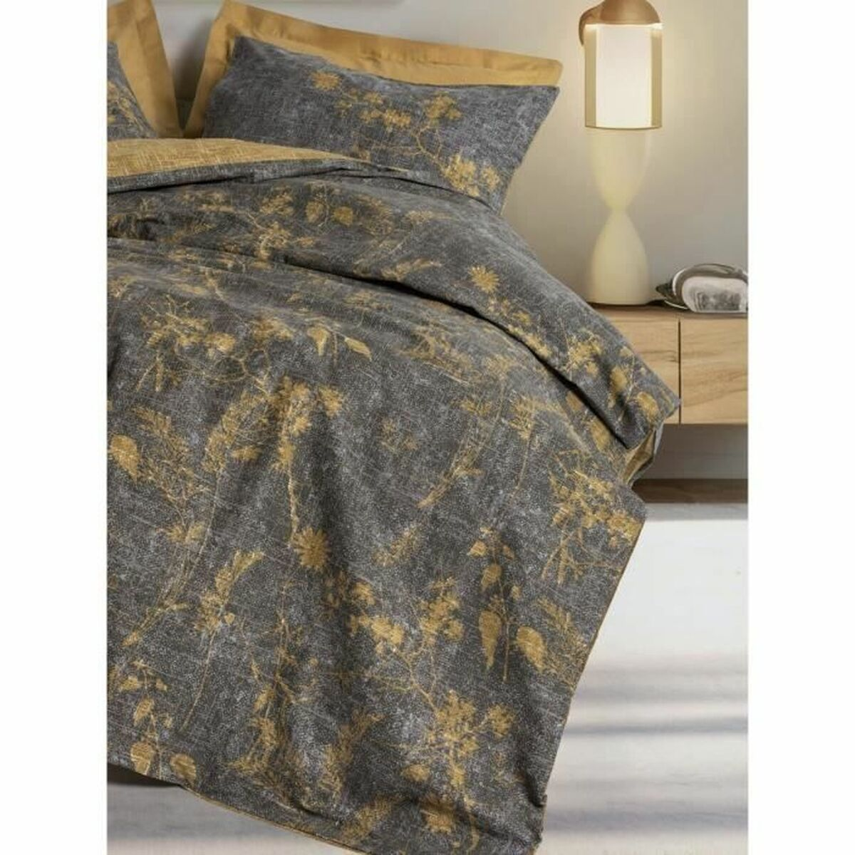 Bettwäsche-Set mit grau-goldenem Blumenmuster auf Bettbezug und Kissenbezügen. Das Bett ist mit neutralfarbenen Laken bezogen.