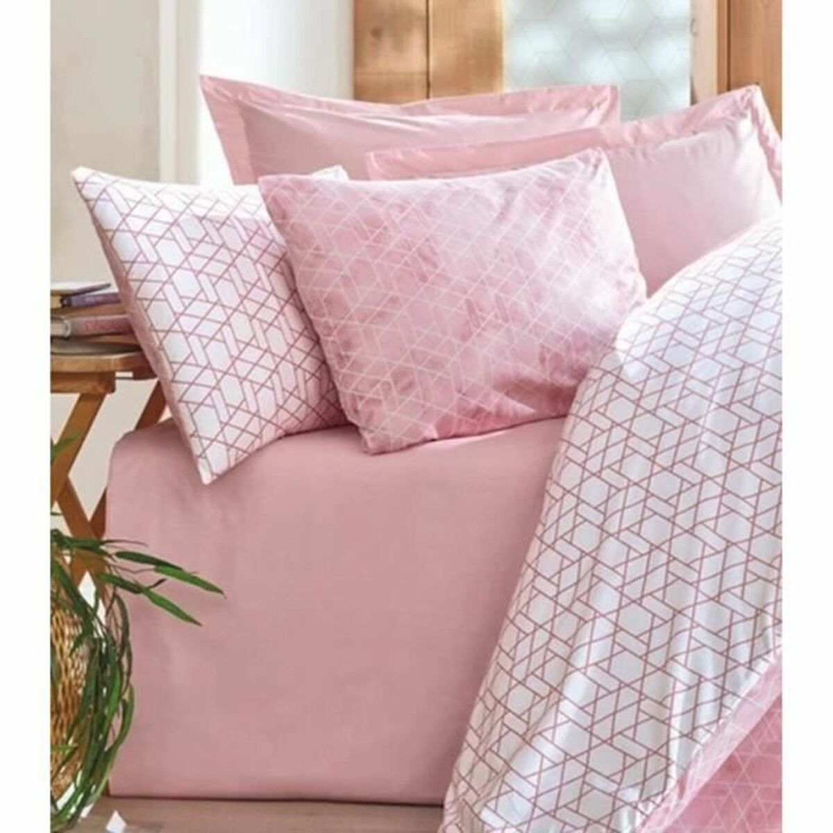 Ein Bett mit rosa Bettwäsche und gemusterten Kissen. Ein kleiner Beistelltisch ist sichtbar.