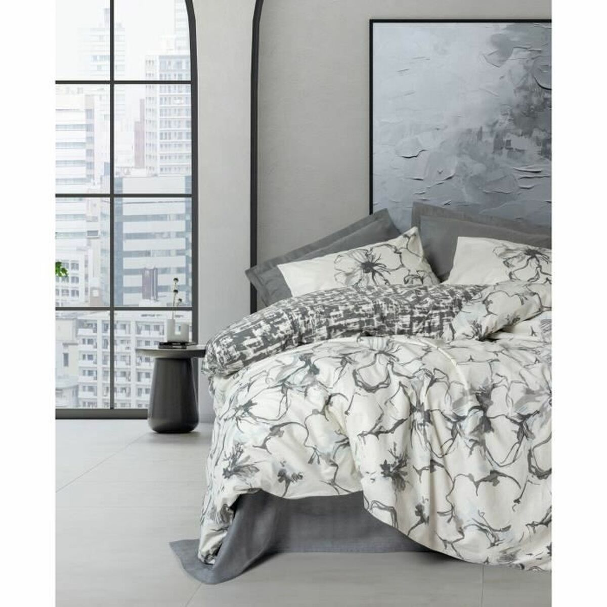 Weißes Bettwäsche-Set mit grauem Blumendesign. Kissen und Bettdecke sichtbar. Großes Fenster im Hintergrund.