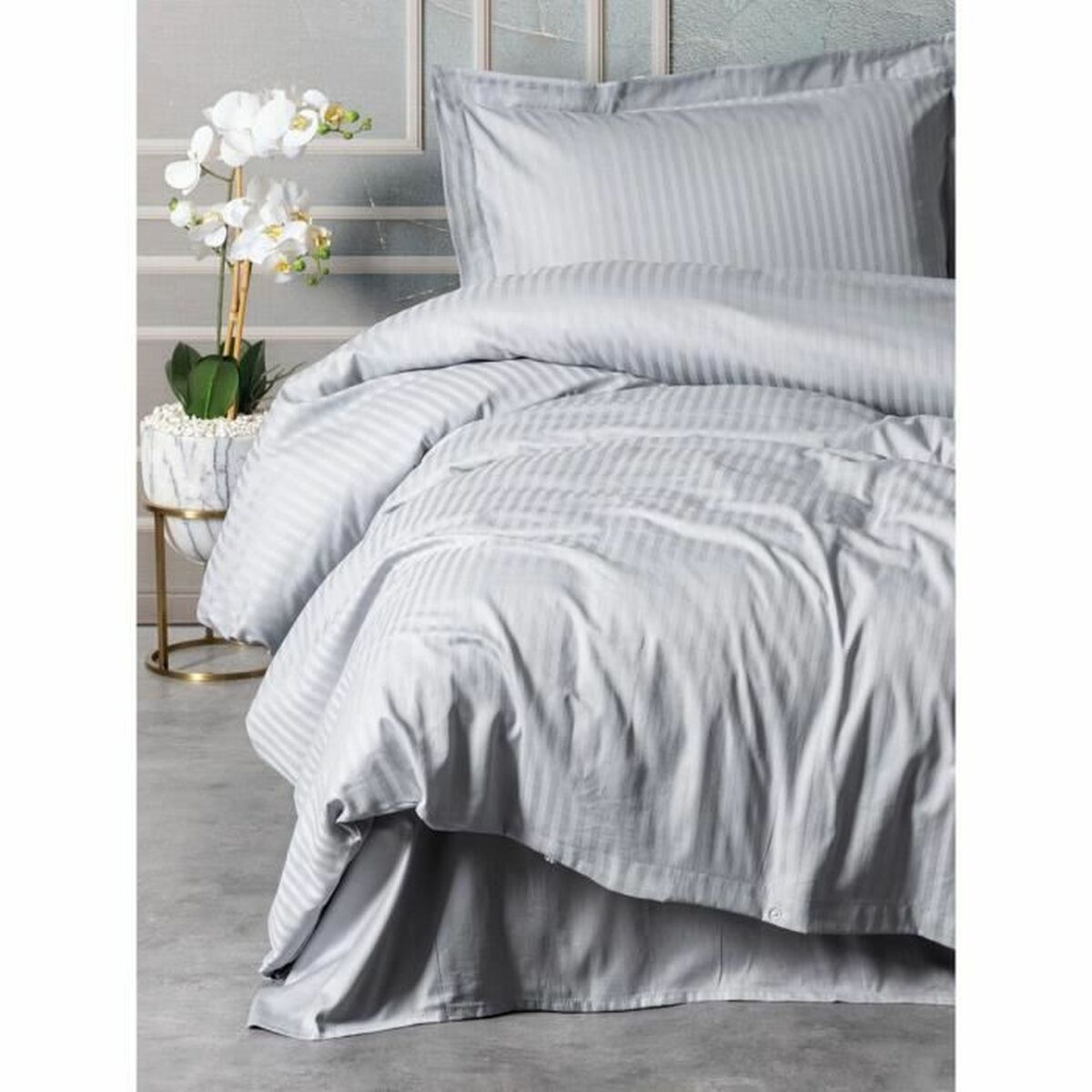 Schlafzimmer mit einem Bett mit grau gestreifter Bettwäsche. Weiße Blumen auf einem Tisch. Graue Wände und Boden.