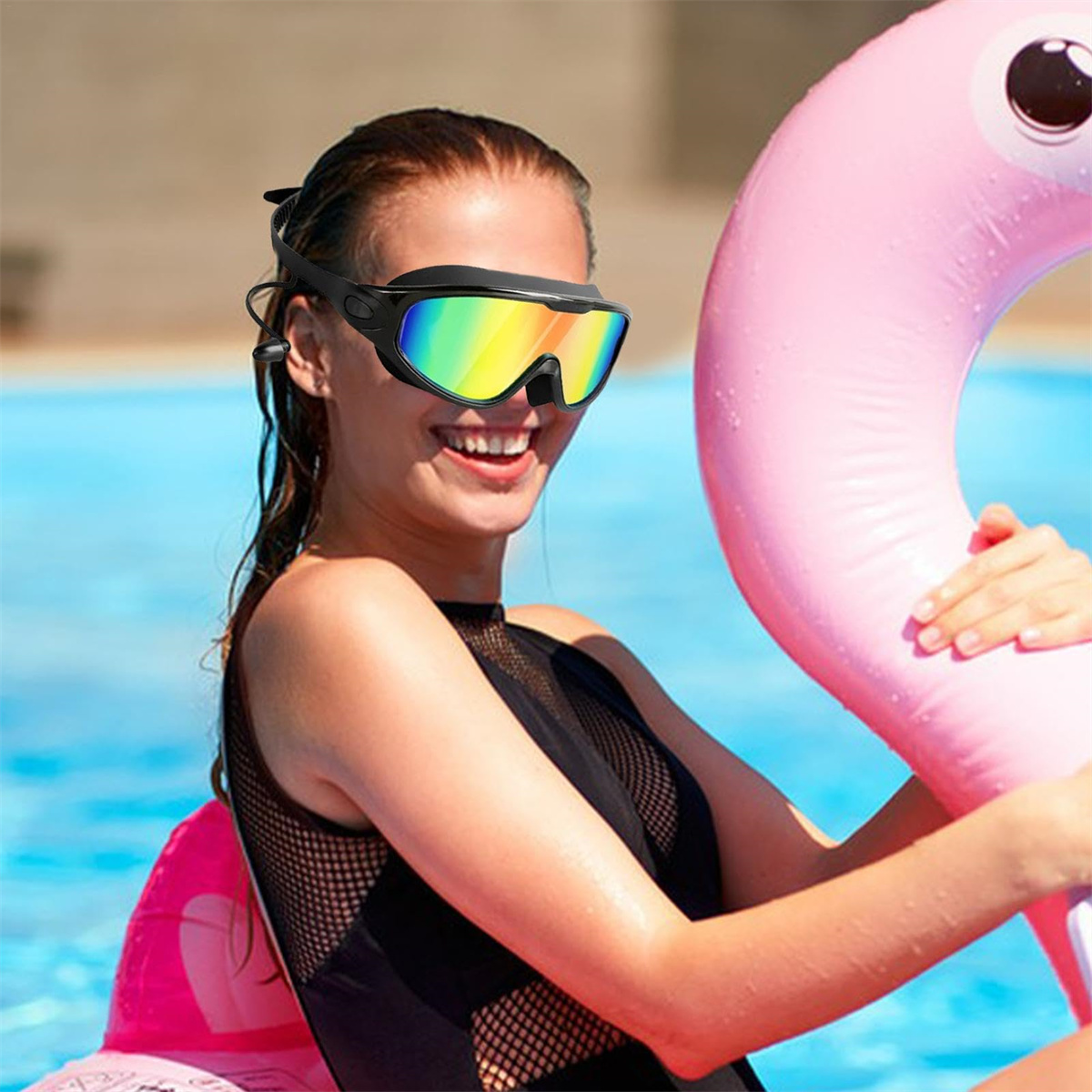 Frau hält eine rosa Flamingo-Luftmatratze und trägt eine schwarze Schwimmbrille mit Regenbogenlinsen, lächelt am Pool.