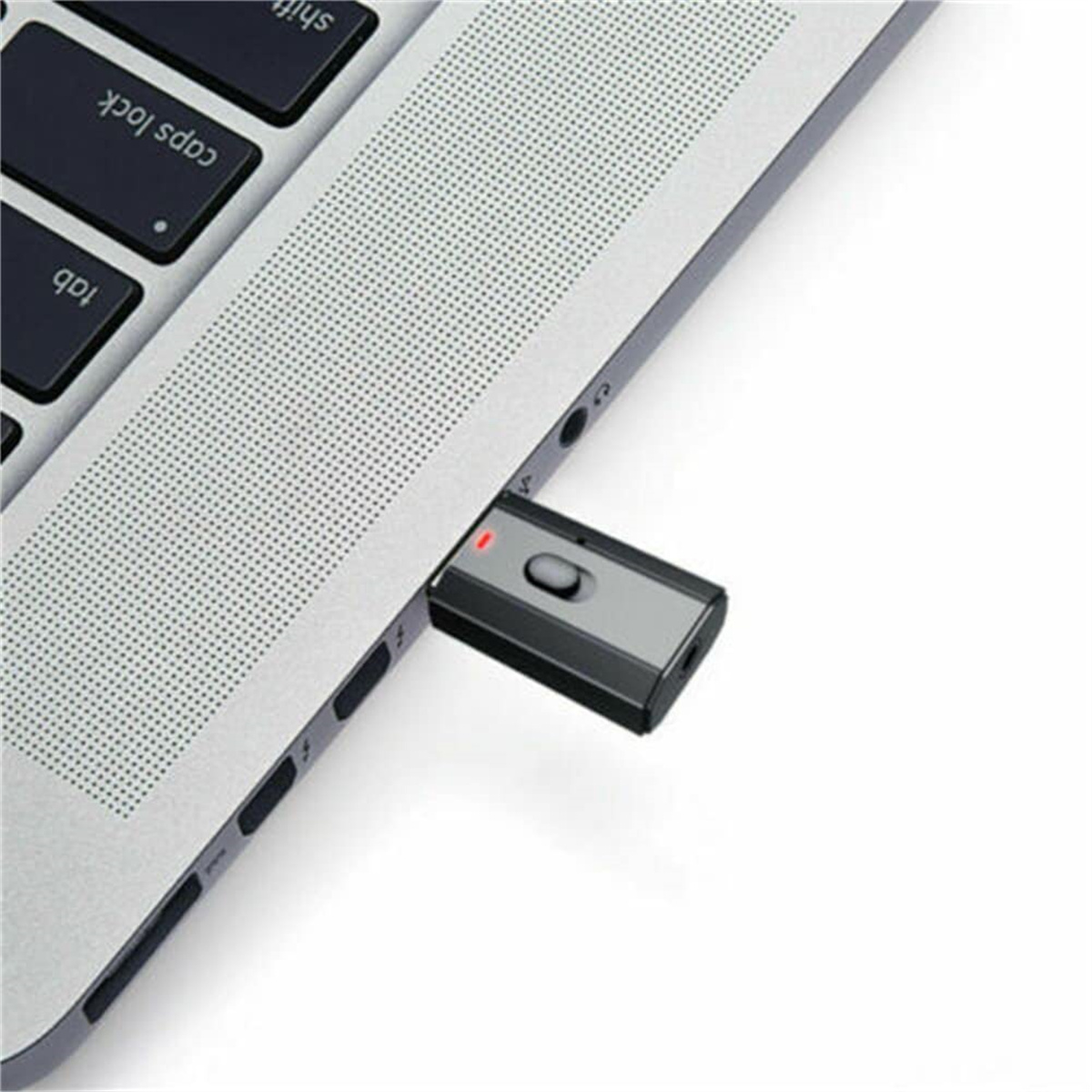 Ein grauer USB-Bluetooth-Adapter, der an einen Laptop angeschlossen ist. Der Laptop ist silber. Der Hintergrund ist weiß.