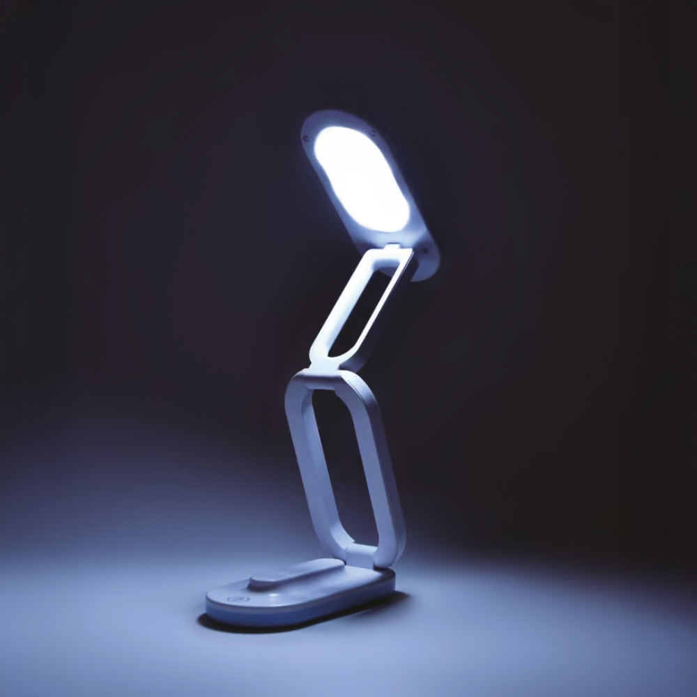 Una lampada LED pieghevole bianca e blu è accesa. È su una superficie bianca, che proietta una luce blu in un ambiente scuro.