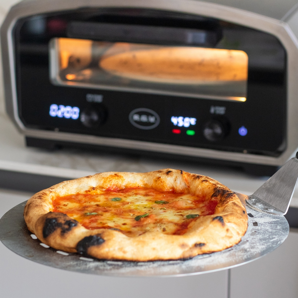 Pizza wird mit einem Metallspatel aus einem Pizzaofen genommen. Die Pizza hat Käse und Soße.