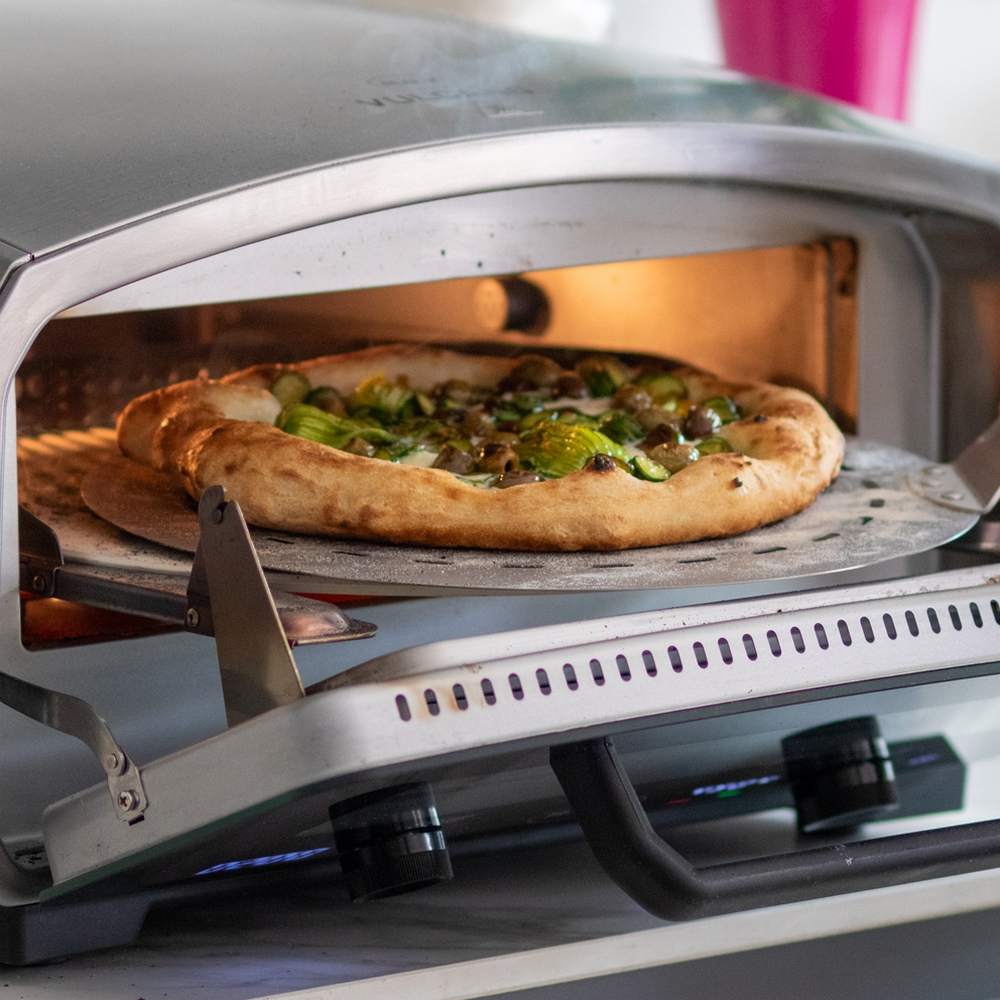 Pizza mit Zucchiniblüten und Käse wird aus einem Pizzaofen genommen. Pizza auf einem Pizzaschieber.