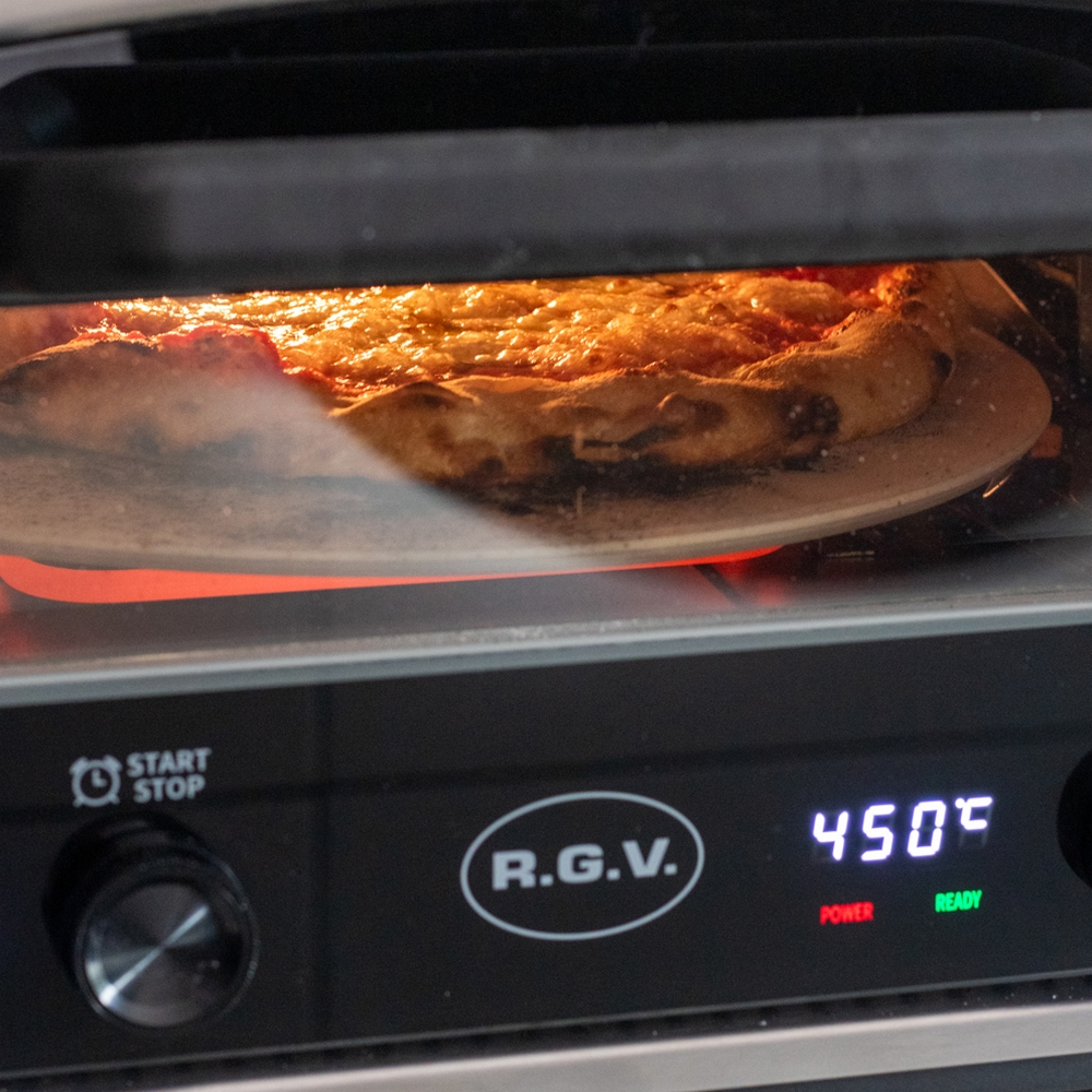 Nahaufnahme einer Pizza in einem Ofen. Die Pizza hat geschmolzenen Käse und liegt auf einem Steinboden. Der Ofen zeigt 450 Grad.
