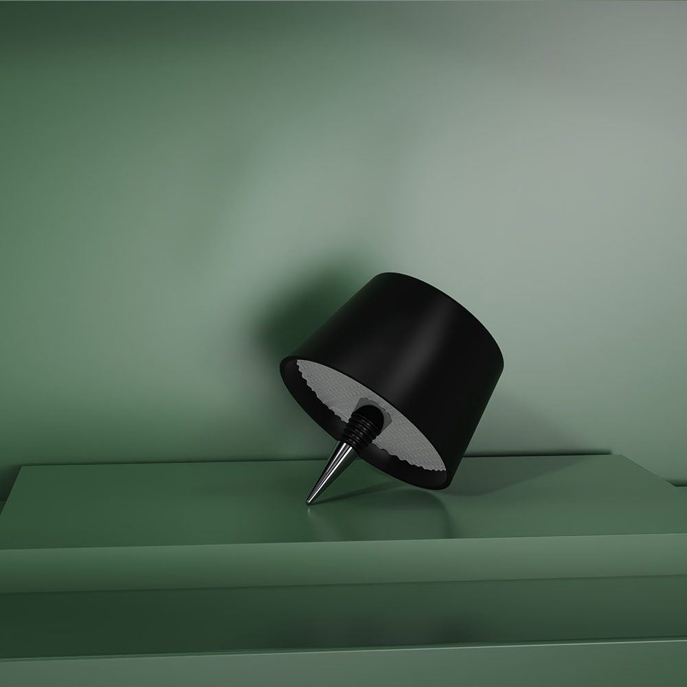 Tappo per lampada nero appoggiato su mensola verde. Lo sfondo è verde chiaro.