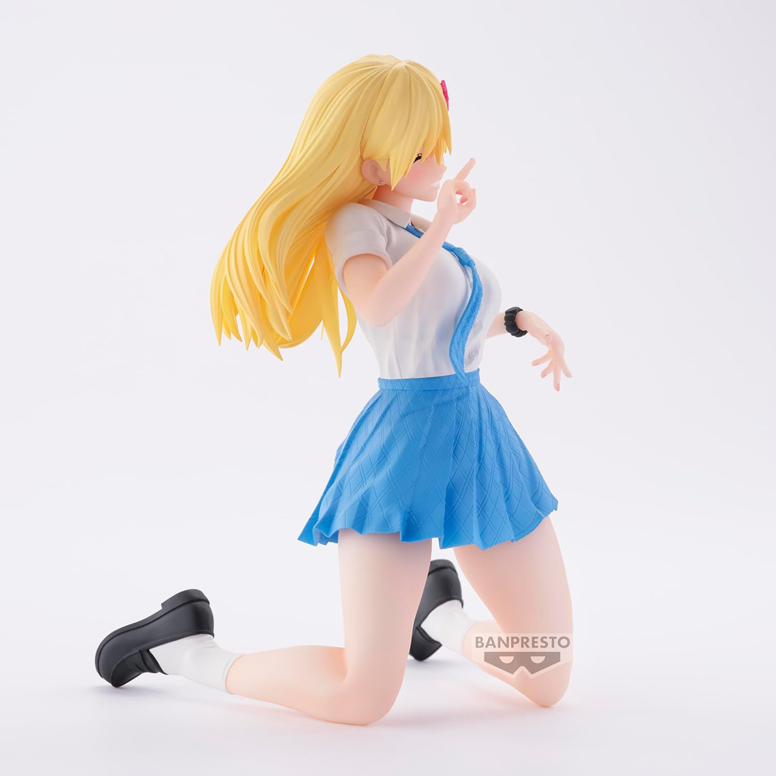 Figura anime de una chica rubia en uniforme escolar, arrodillada, señalando con el dedo.