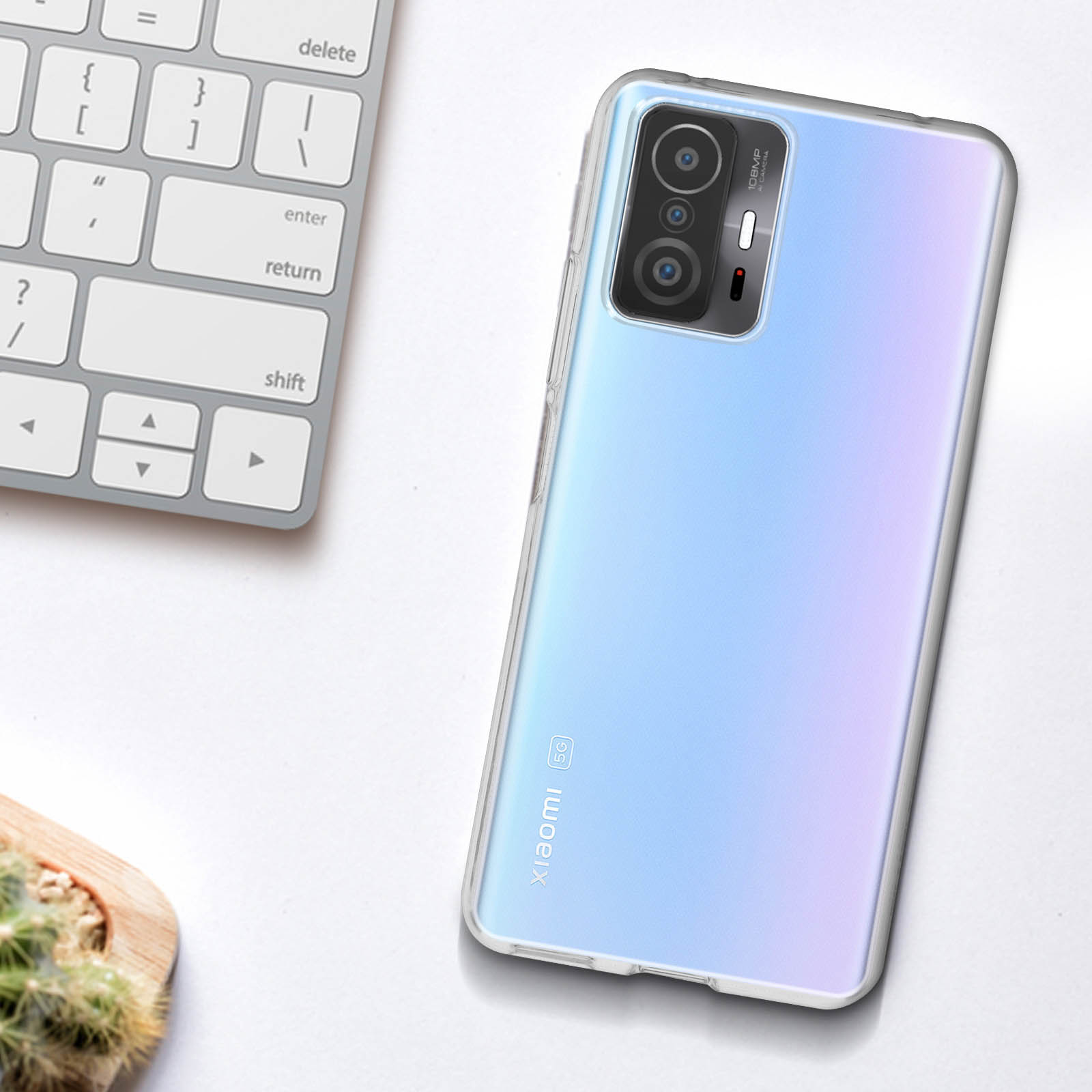 Smartphone con custodia trasparente su un tavolo. Tastiera e pianta sullo sfondo.