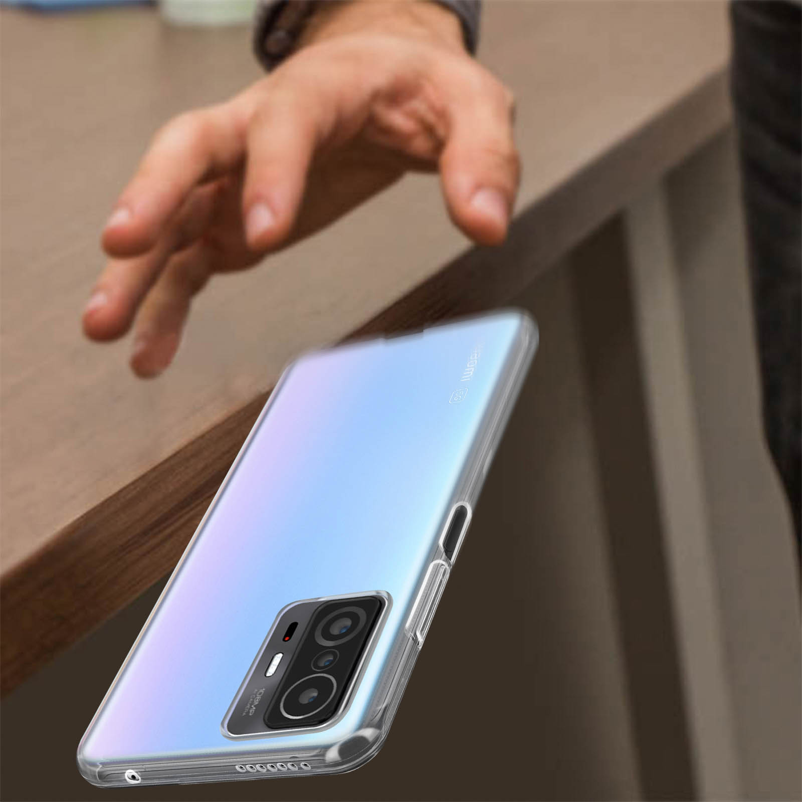 Mano che raggiunge uno smartphone con custodia trasparente su un tavolo. Sfondo sfocato.