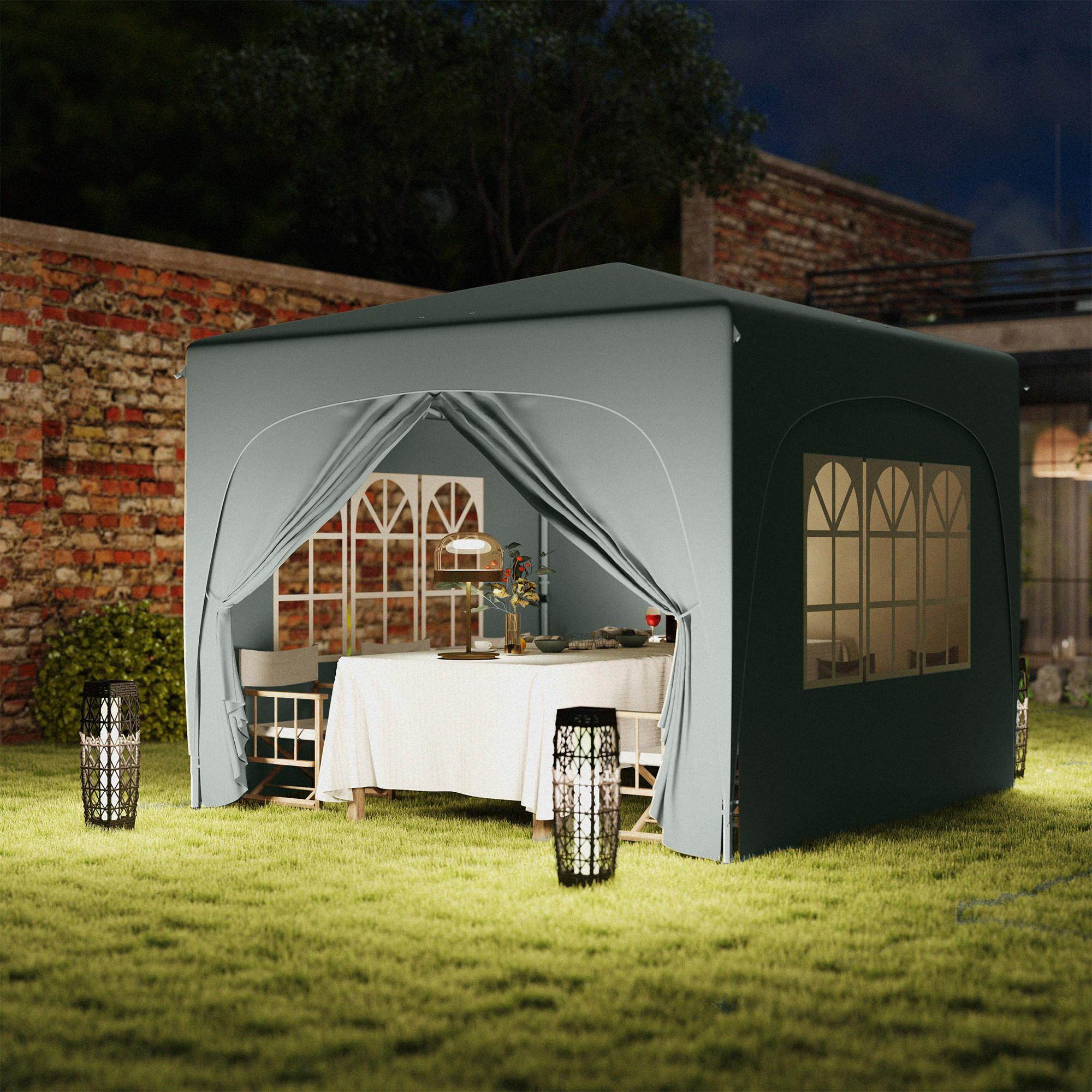 Ein grauer Pavillon bei Nacht mit Tisch. Zwei Laternen stehen auf dem Gras.