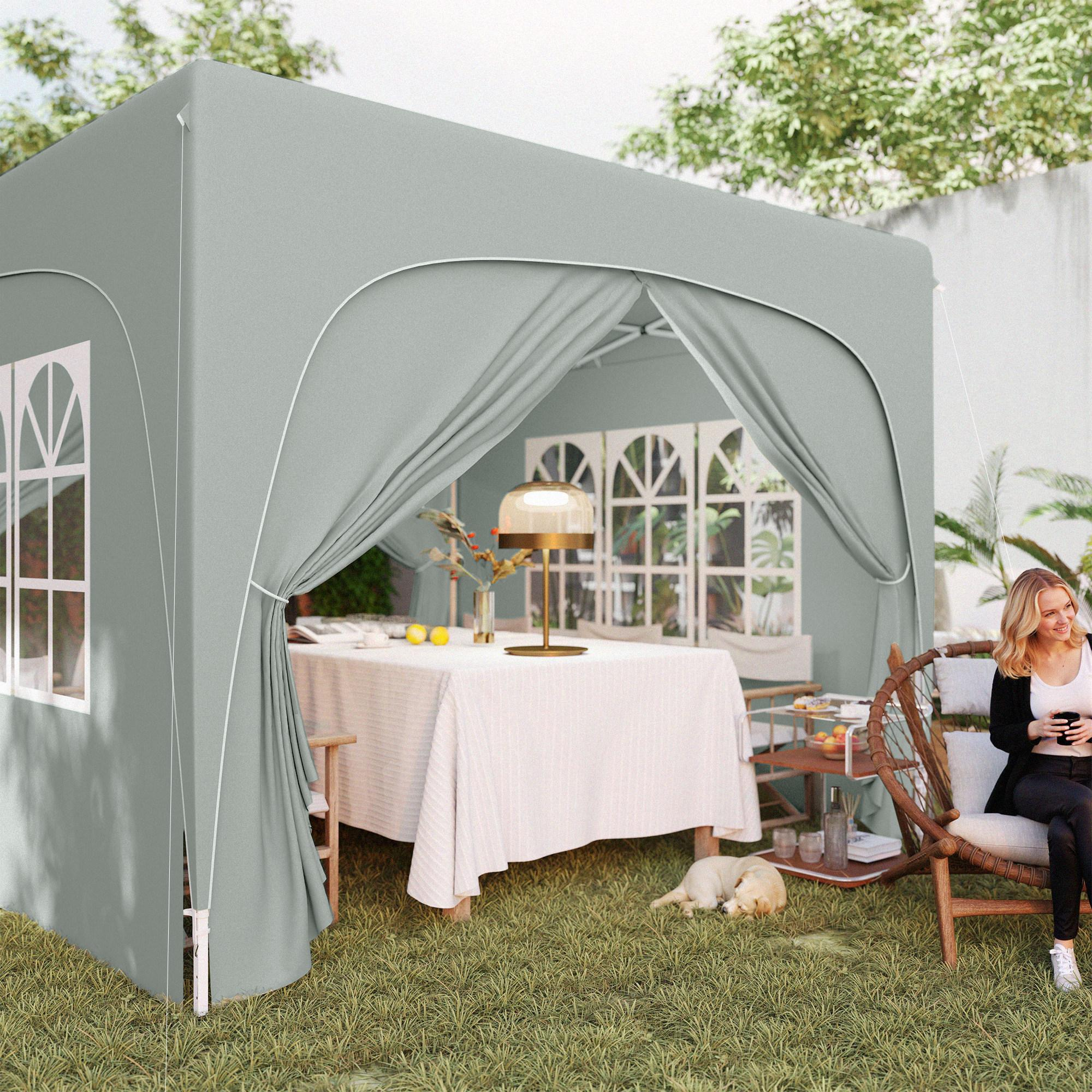 Ein grauer Pavillon mit Tisch und Stühlen. Eine Frau sitzt draußen und trinkt ein Getränk.
