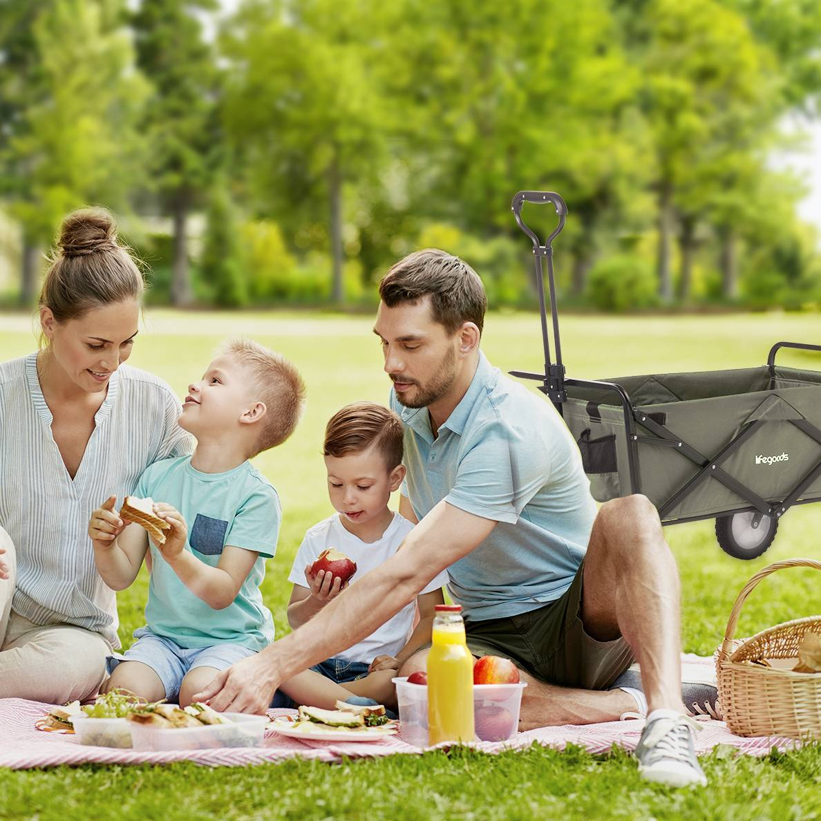 Family picnic on grass. Parents, children, food, and a wagon in the background.