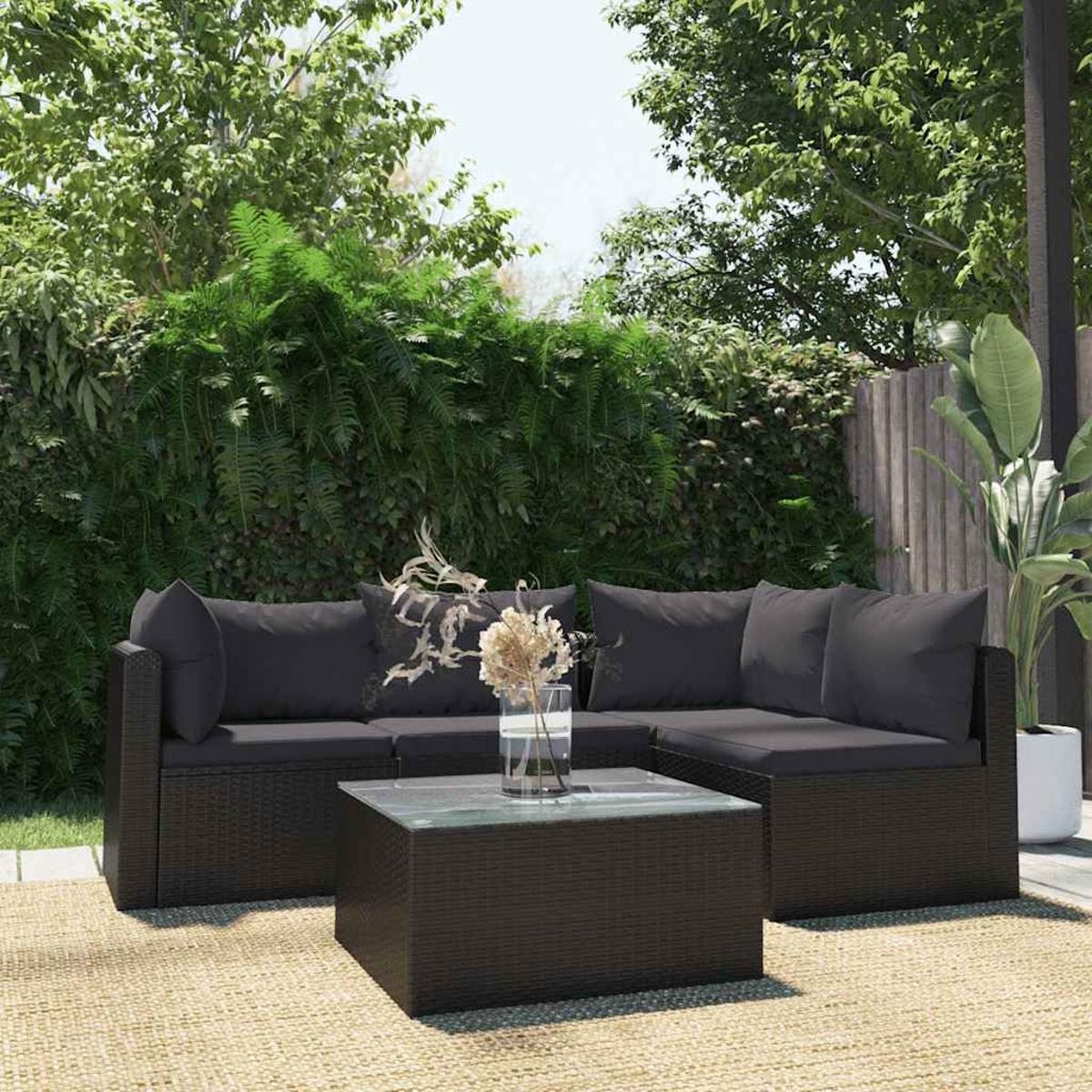 Ein schwarzes, gewebtes Ecksofa und Couchtisch aus Rattan auf einer gewebten Matte, mit Grün im Hintergrund.