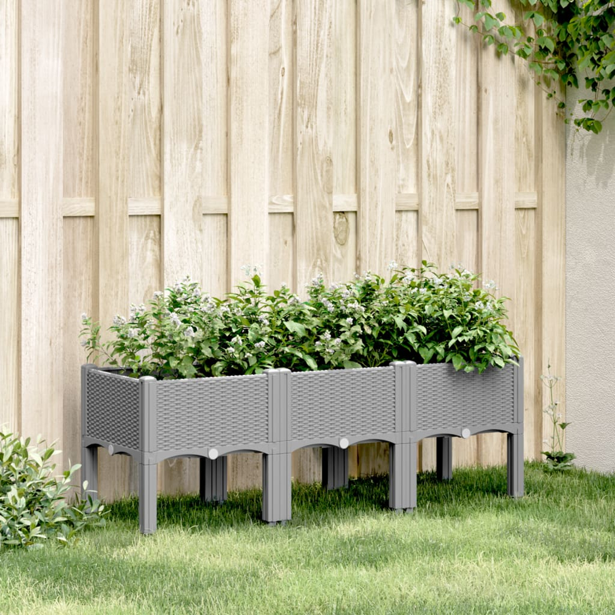 Ein grauer Pflanzkasten im Woven-Stil mit Pflanzen in einem Garten.