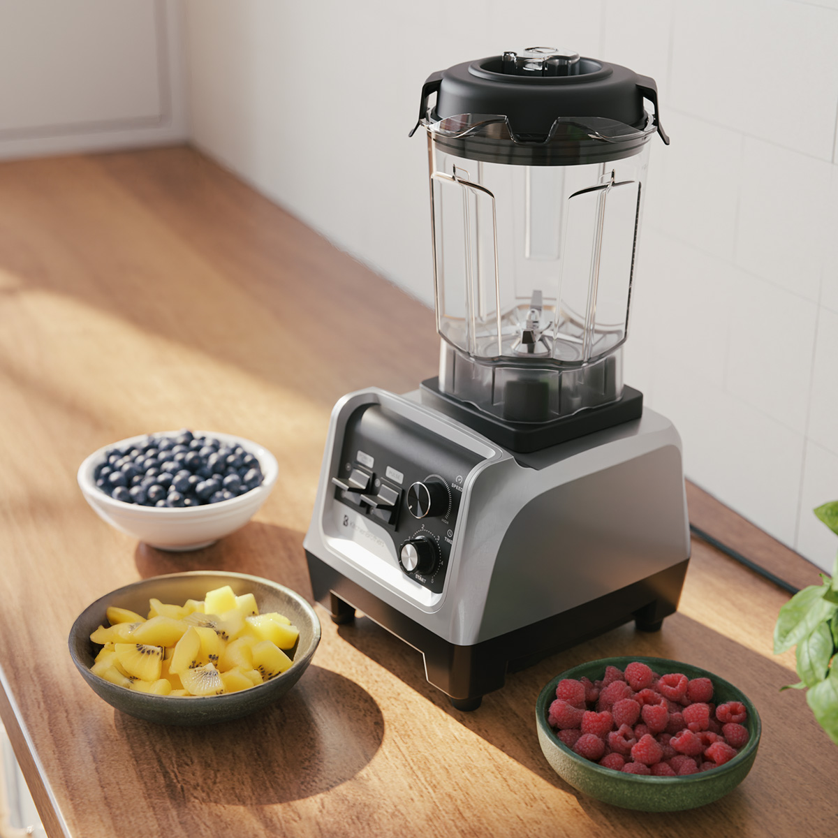 A silver blender with a clear pitcher sits on a wooden counter next to bowls of fruit.