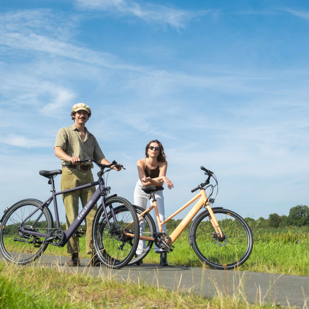 Twee mensen met fietsen op een zonnige dag, blauwe lucht, velden op de achtergrond.