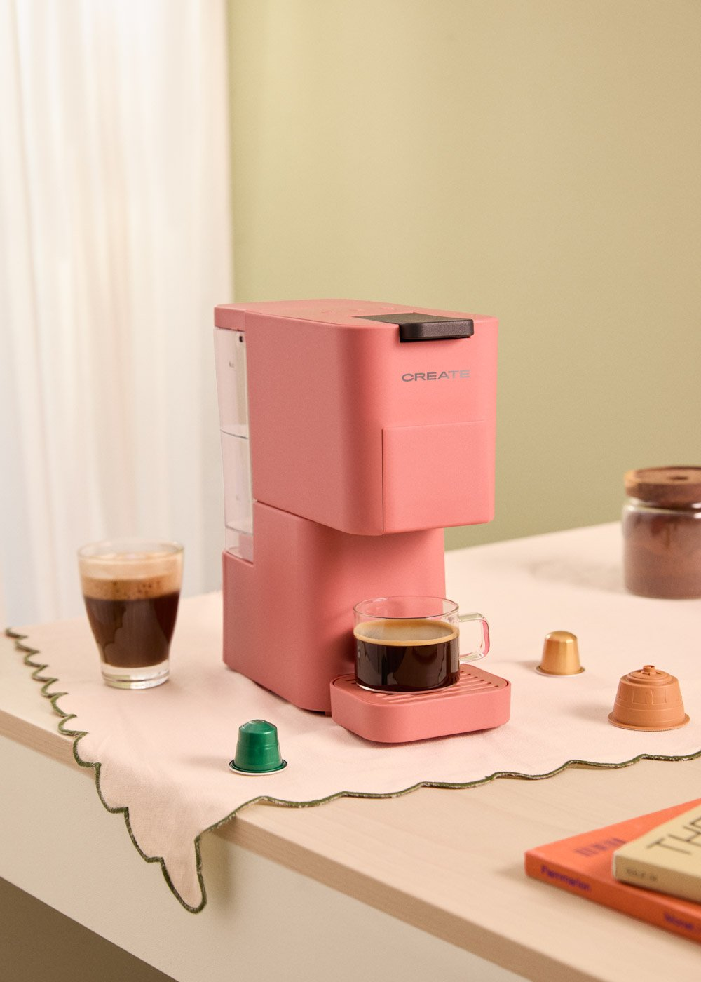 Máquina de café Create rosa con una taza de café y cápsulas en una mesa. Una taza de café a la izquierda.